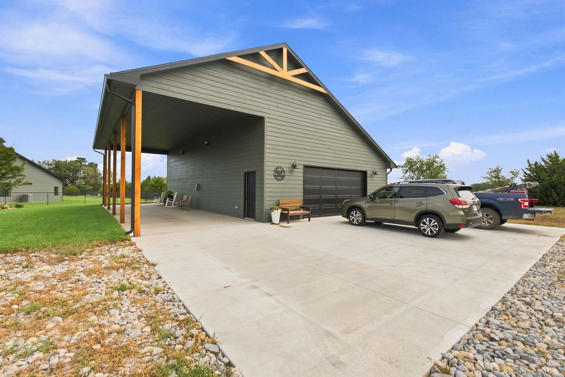 Modern house with large covered driveway, concrete apron, and parked vehicles under a blue sky