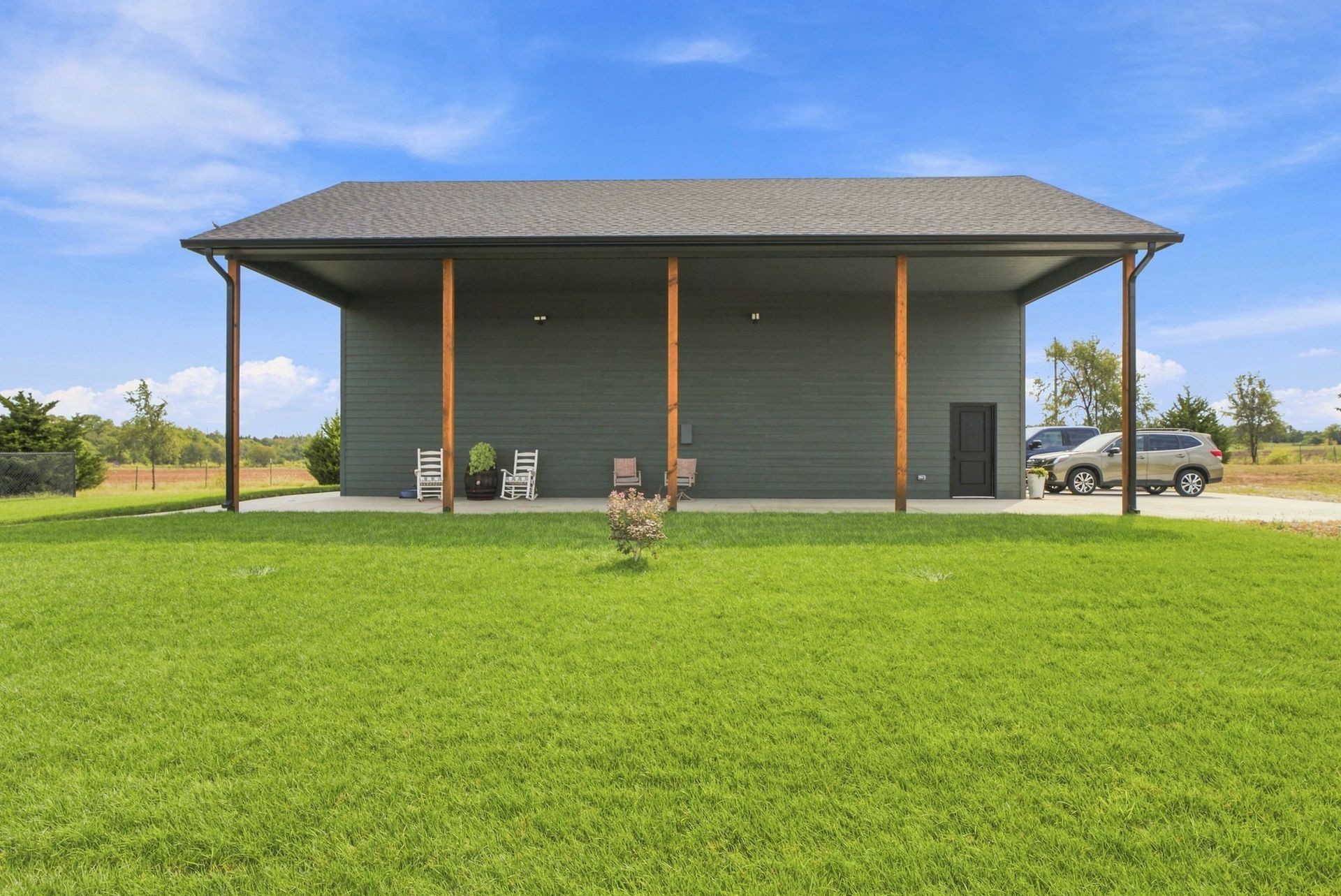 Modern gray house with a covered porch and a large green lawn under a blue sky