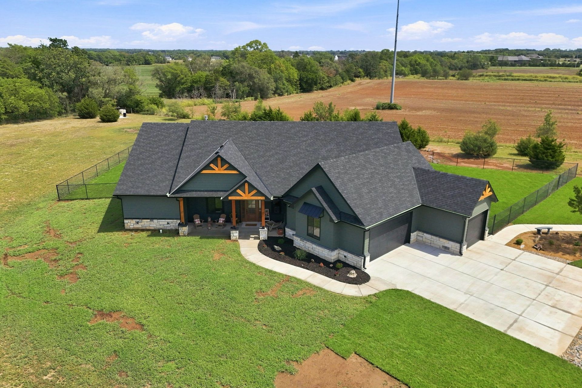 Aerial view of a modern gray house with a driveway, green lawn, and farmland in the background