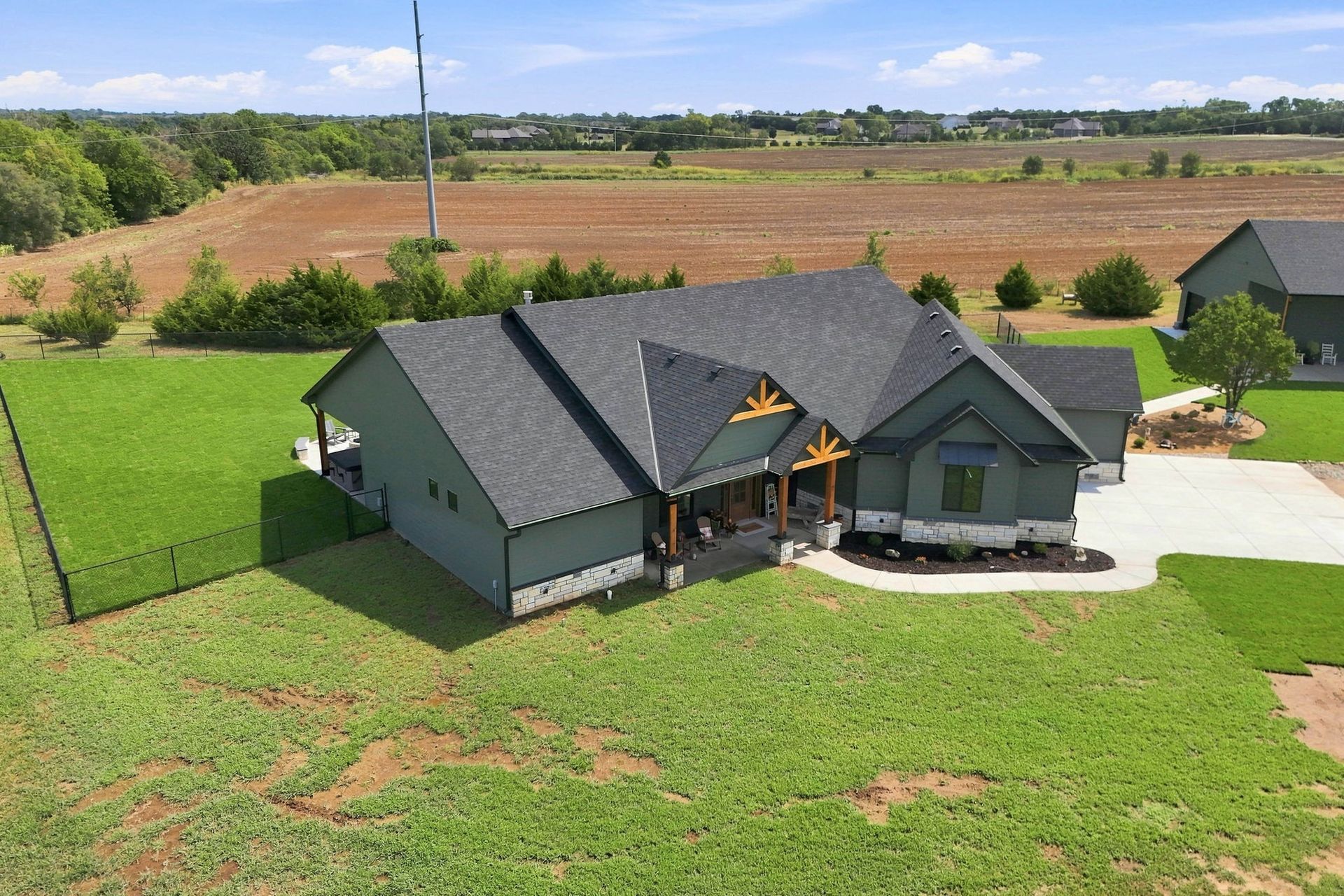 Aerial view of a gray house with a large green lawn and farmland in the background.