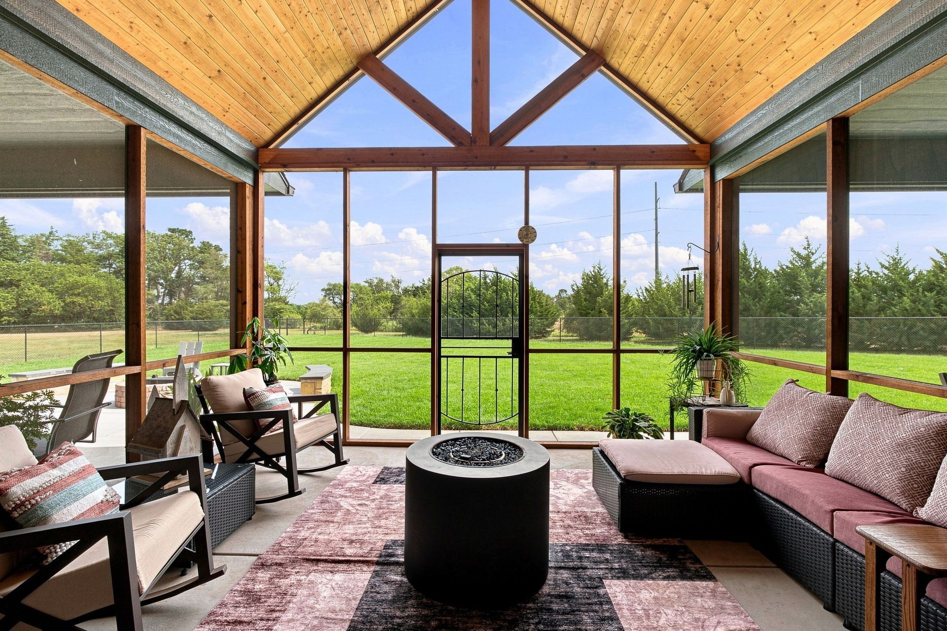 Covered patio lounge with sofas and chairs facing a green lawn through large glass doors