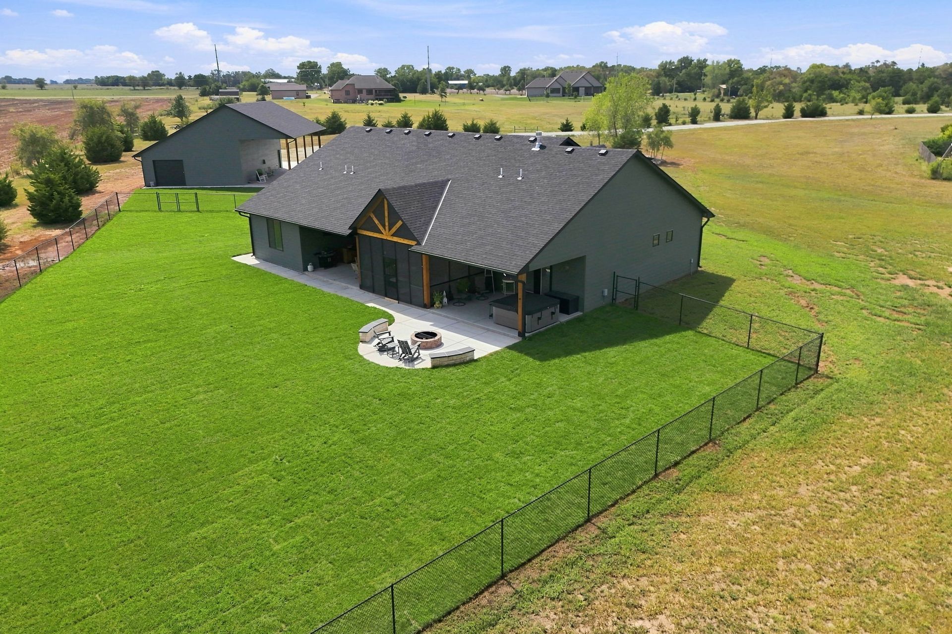 Aerial view of a gray-roofed house with a large green lawn in a rural field.