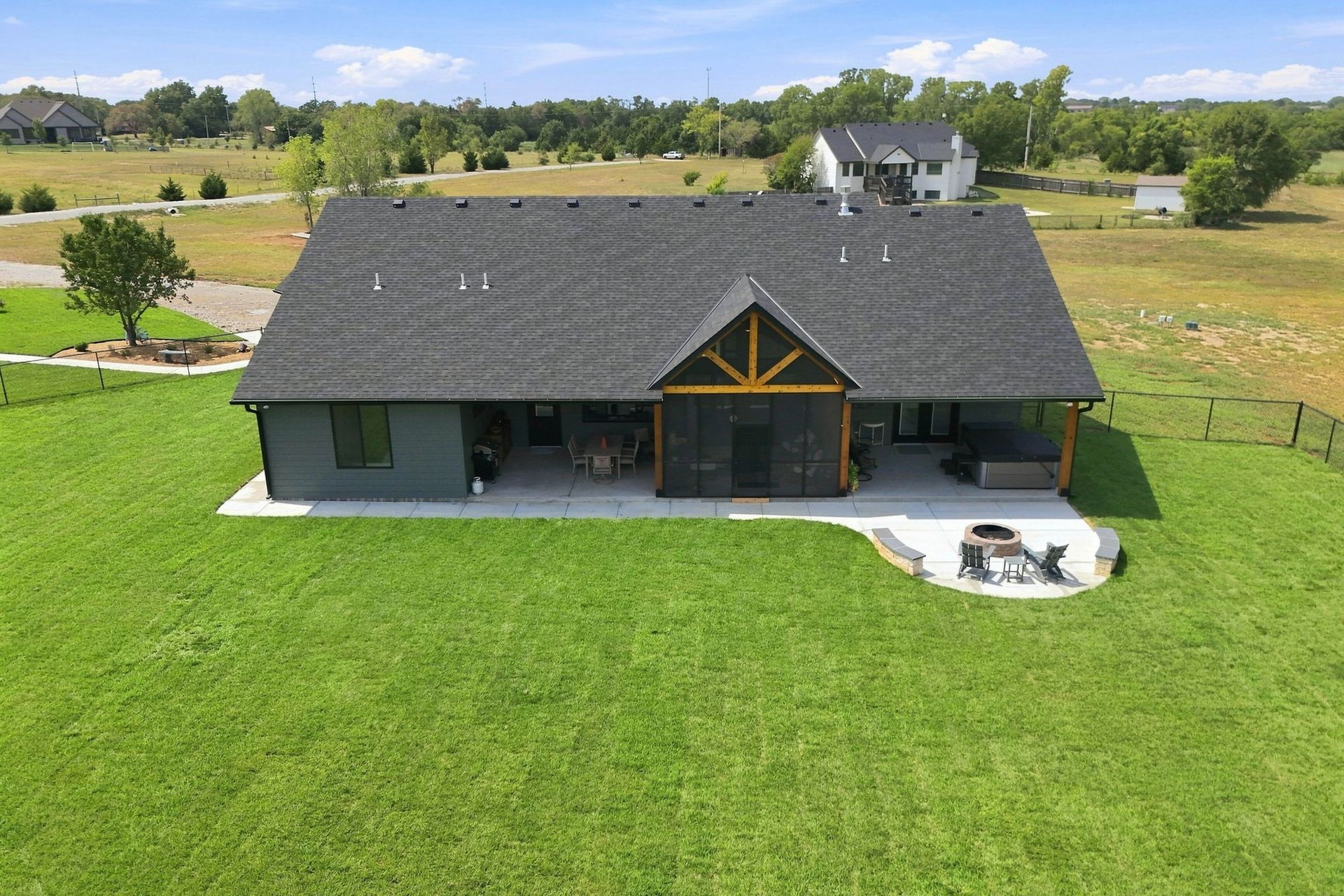 Aerial view of a gray house with a large green lawn and a small patio fire pit area.