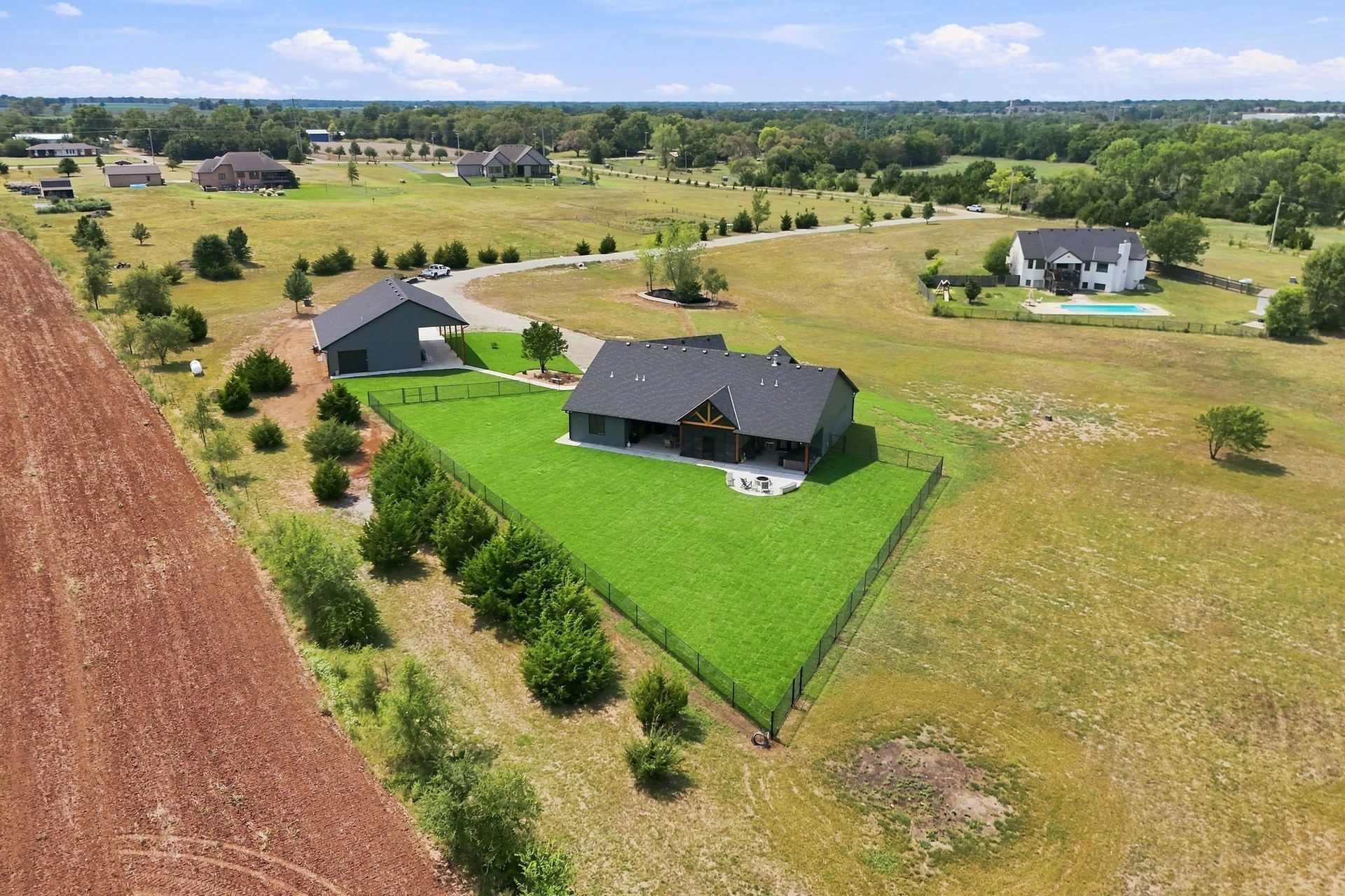 Aerial view of a suburban neighborhood with houses, green lawns, and open fields under a blue sky