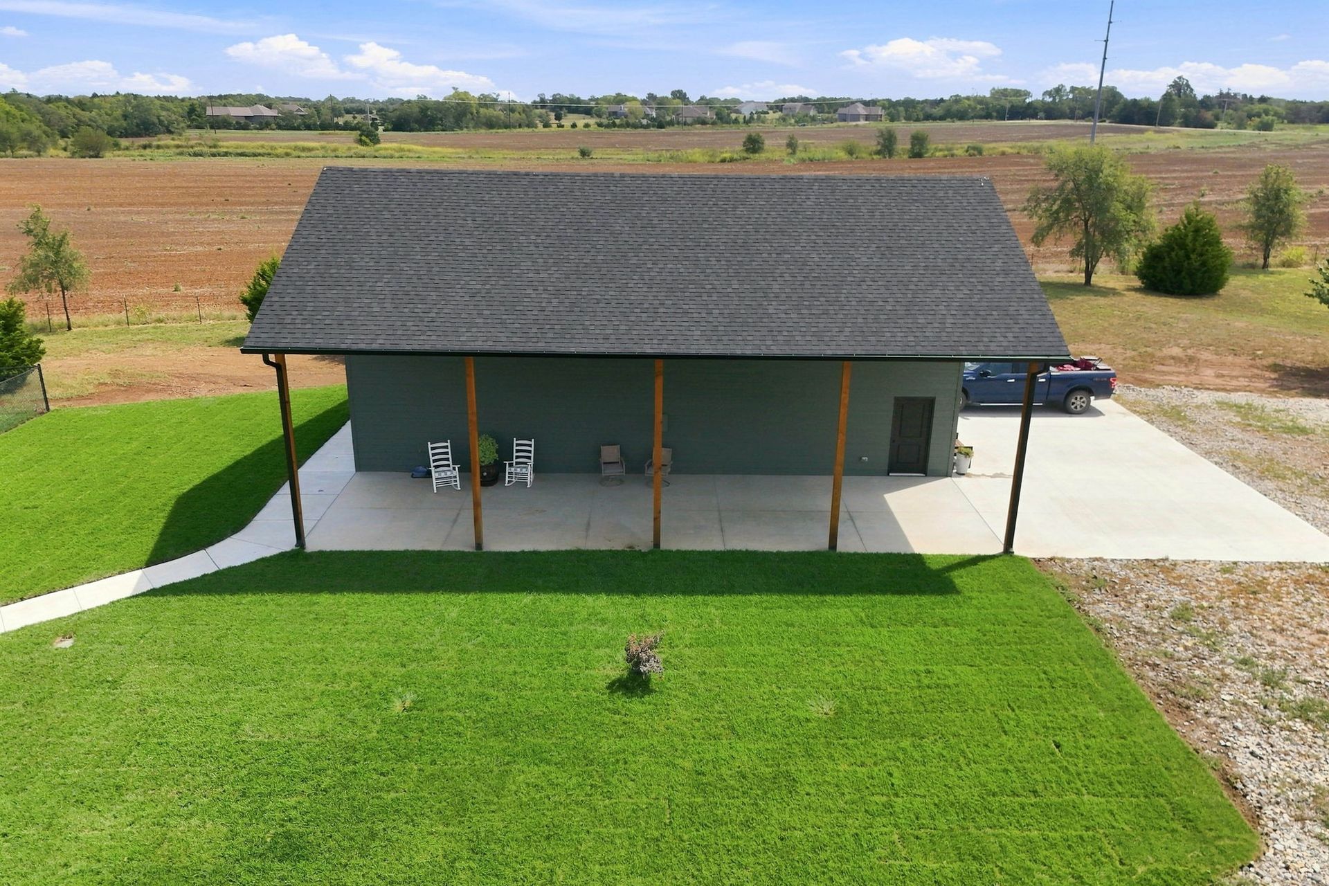 Small gray house with a dark roof, front porch, and bright green lawn in a rural field.
