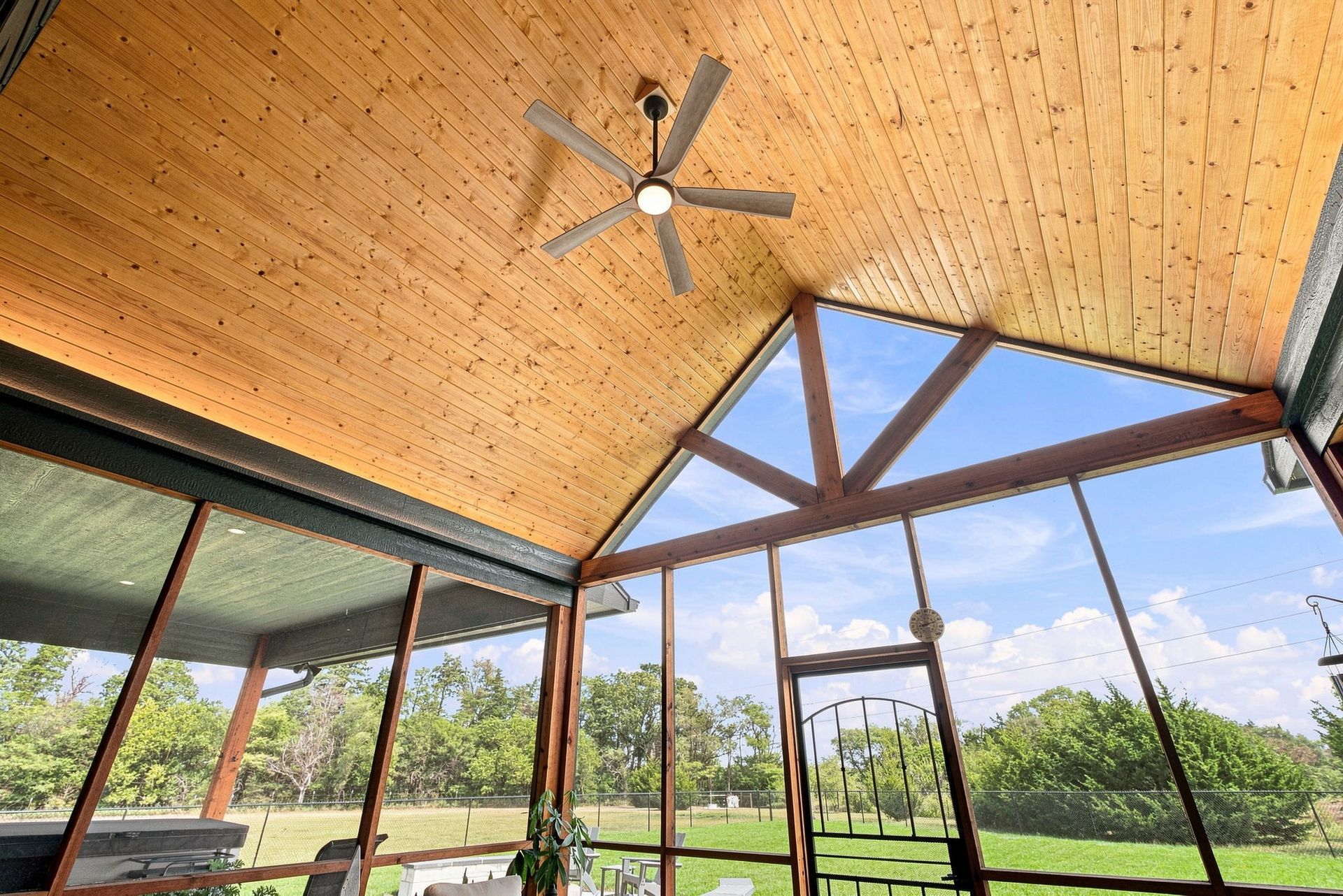 Modern patio with wood ceiling, ceiling fan, and open view of green landscape and blue sky