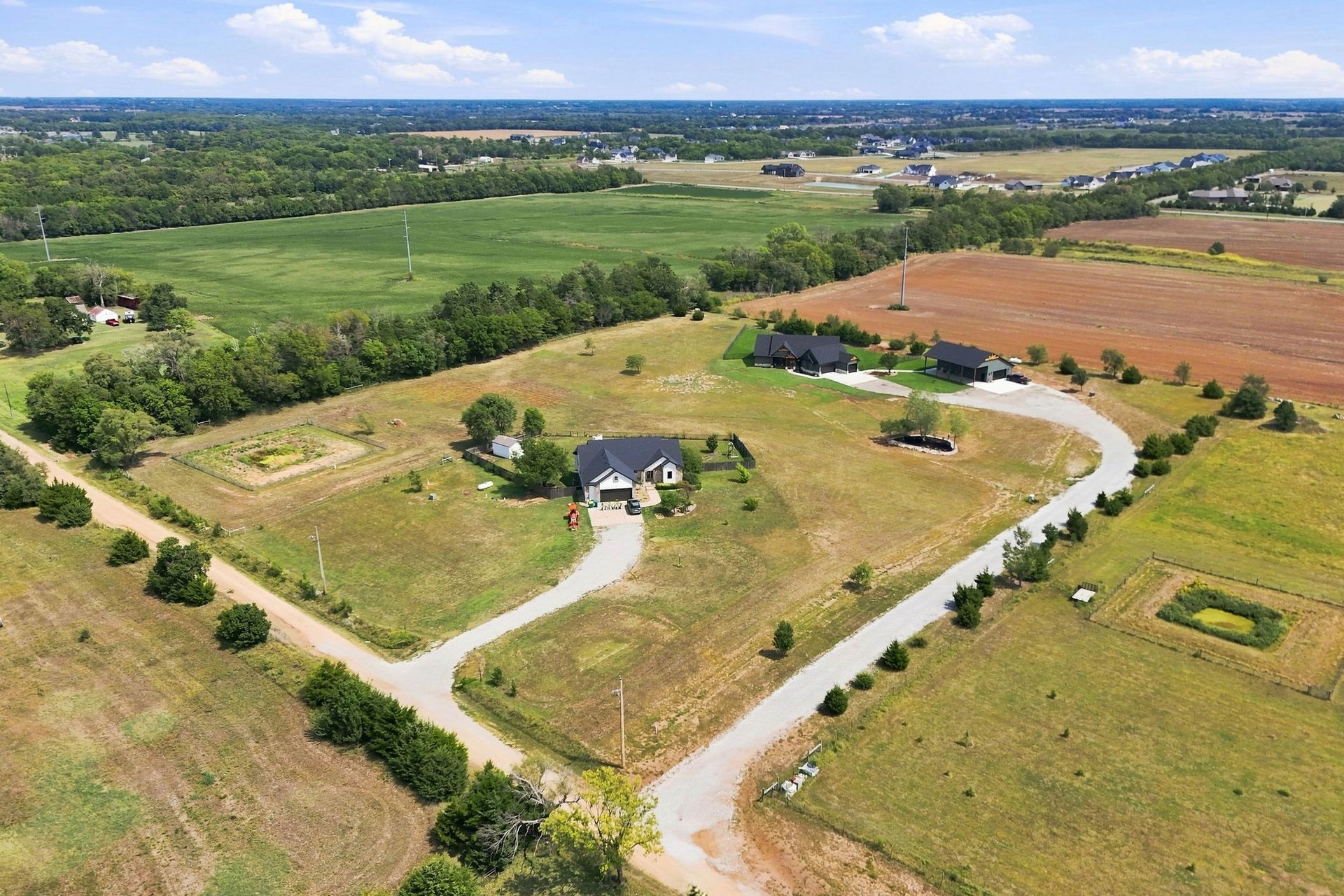 Aerial view of a rural house with winding driveway, surrounded by green fields and open farmland.