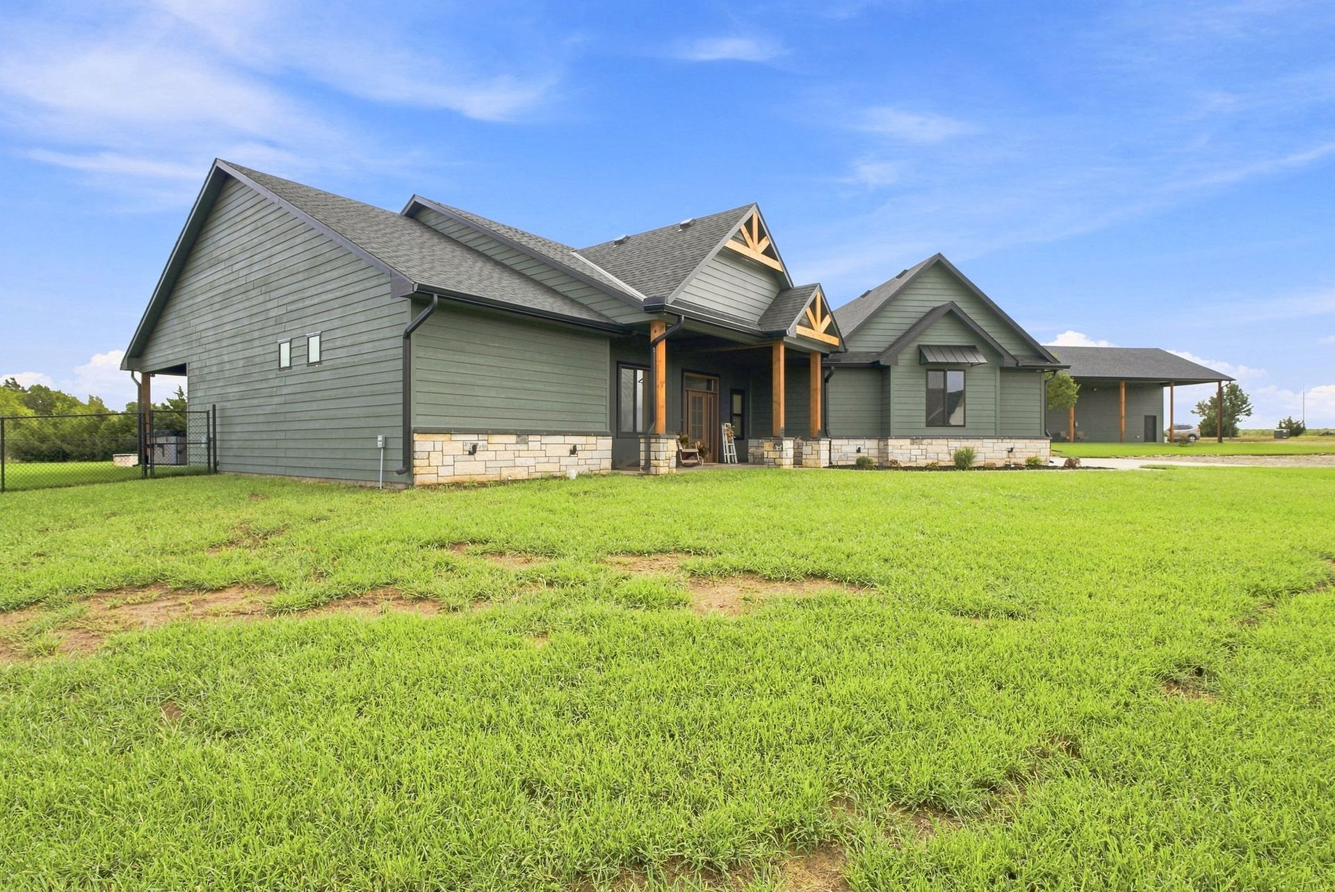 Gray house with a front porch on a large green lawn under a blue sky