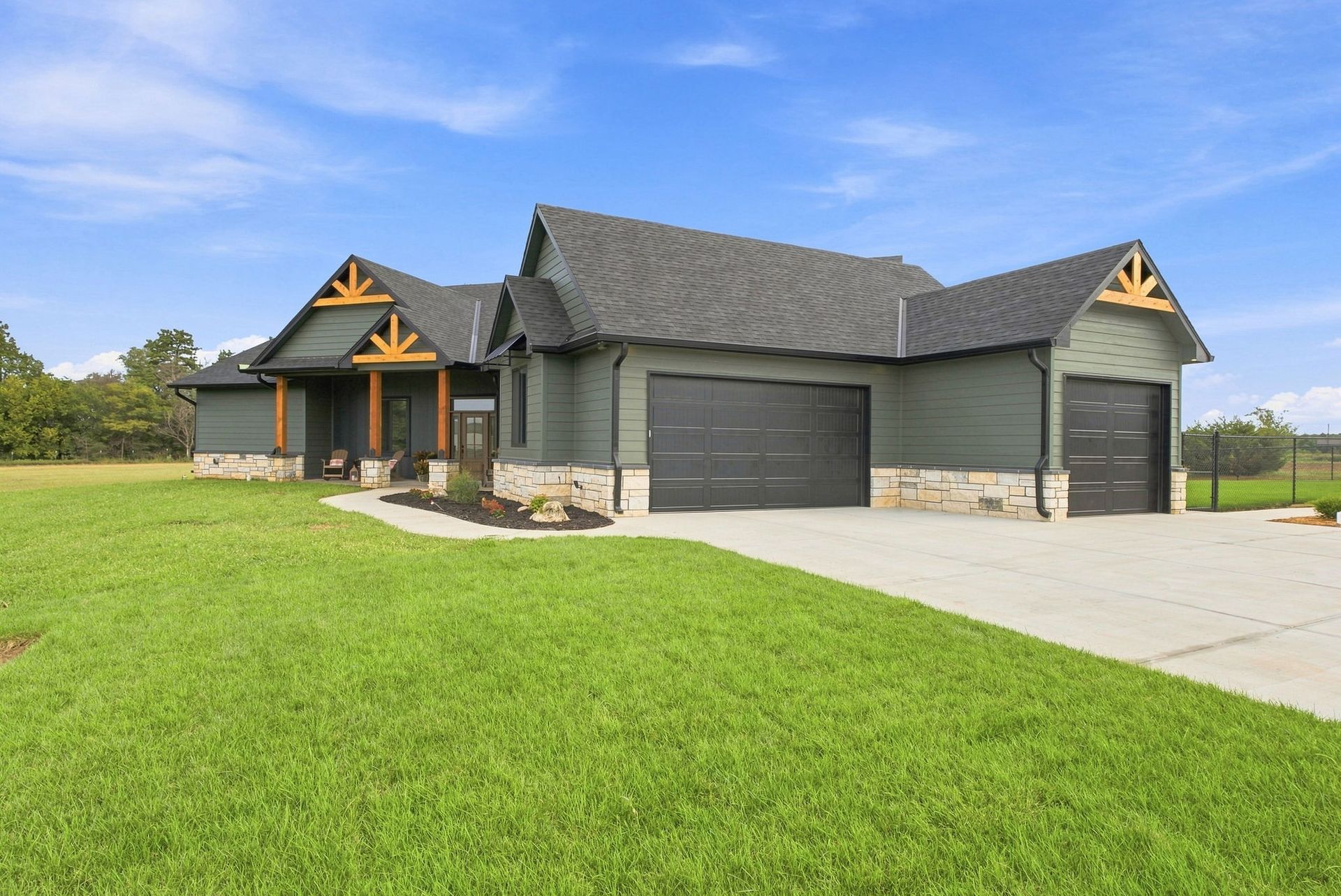 Modern gray house with stone accents, two garage doors, and a large green lawn under a blue sky