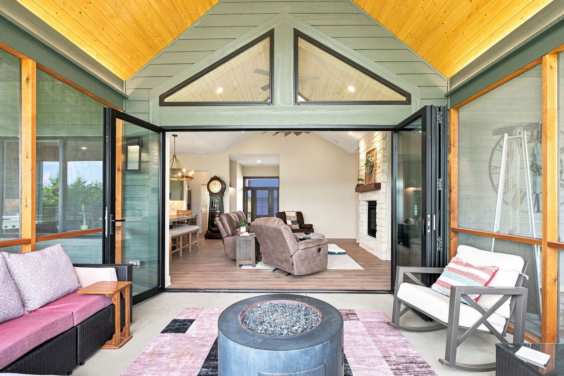 Sunlit screened porch with pink chairs and a round black table opening to a cozy living room
