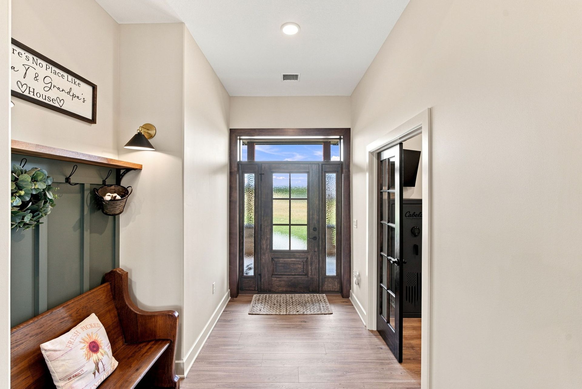 Narrow entry hall with white walls, wood floor, bench, and glass front door with sidelights.