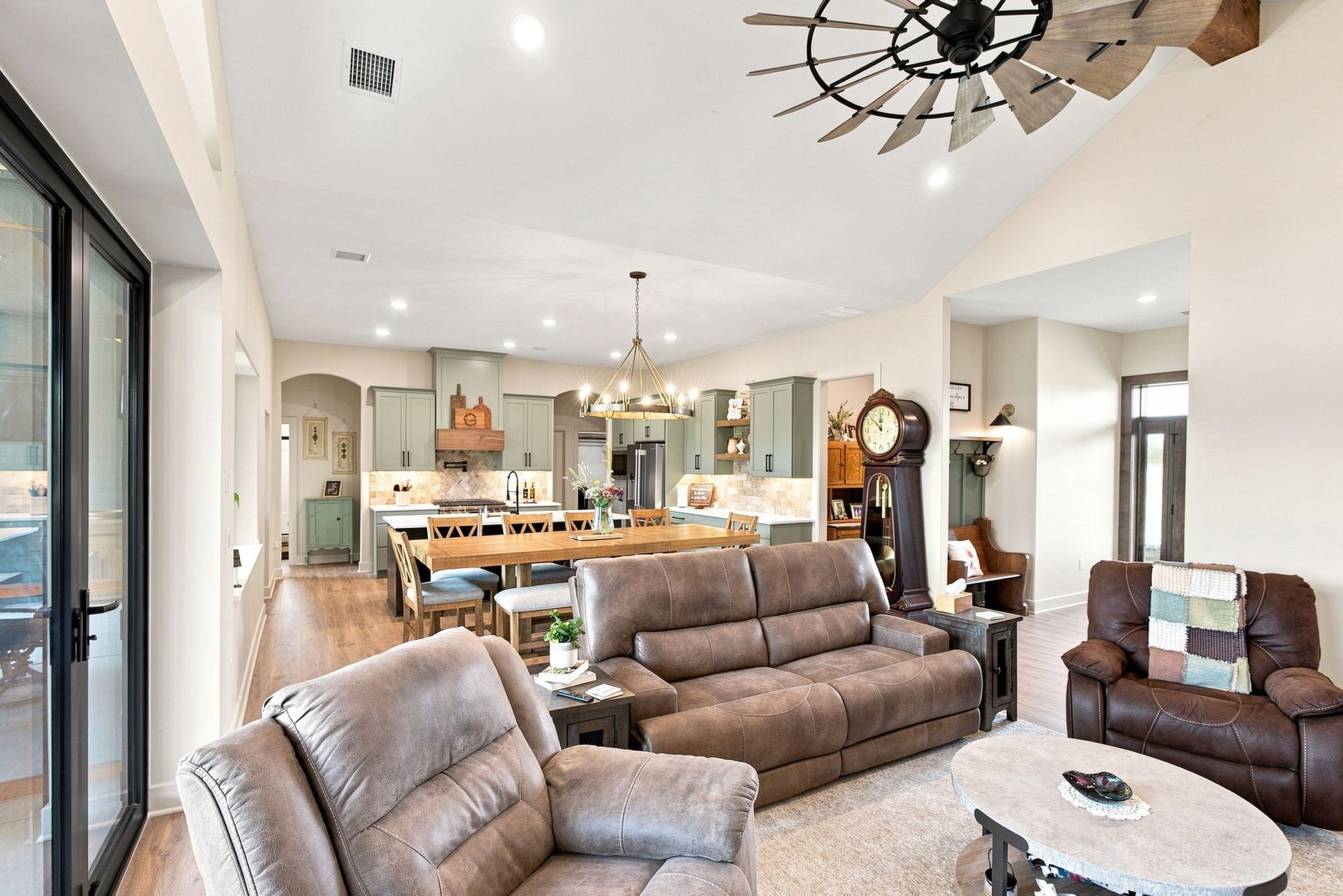 Bright living room with brown sofa, armchairs, dining table, and open kitchen.