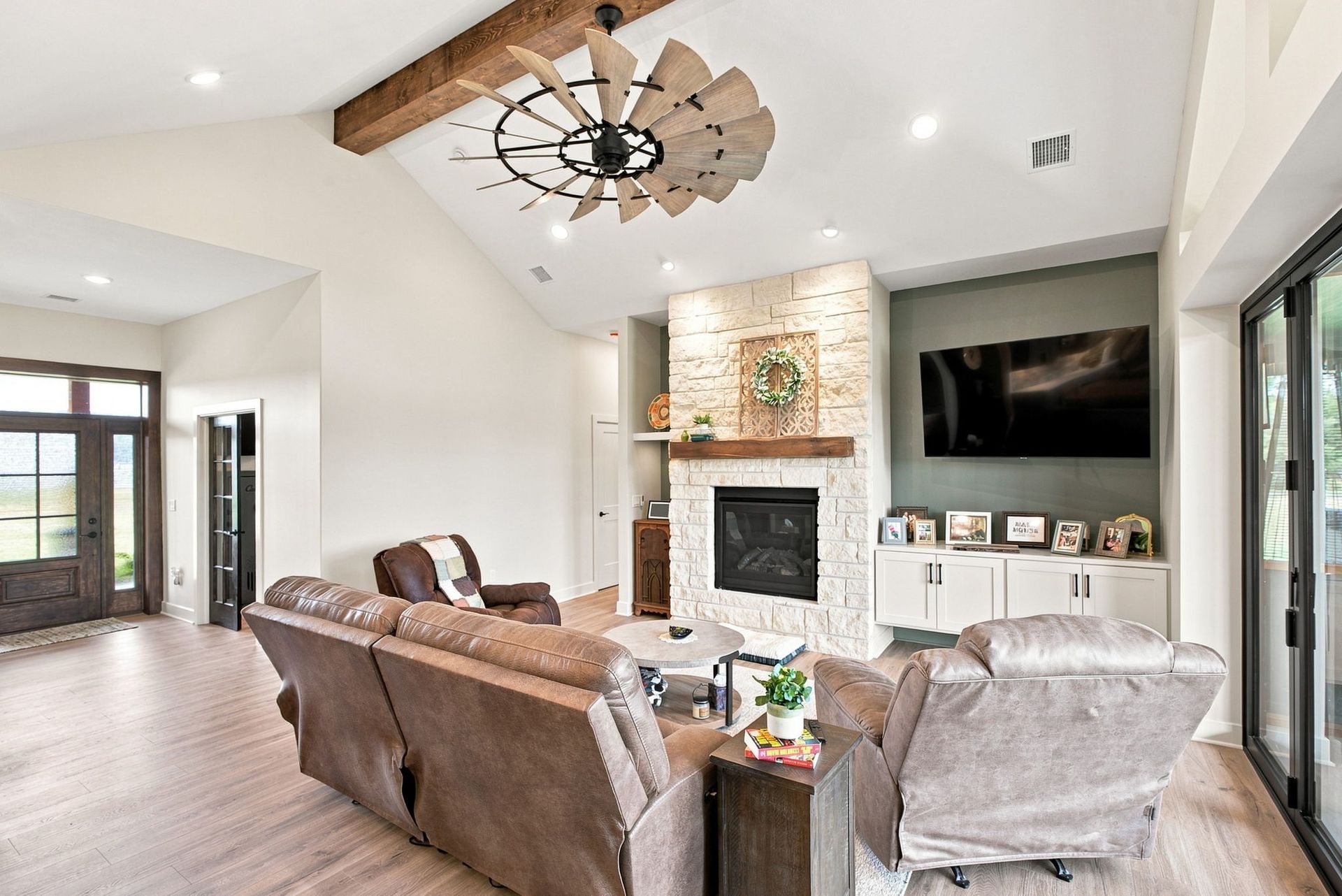 Bright living room with brown sofas, fireplace, wall-mounted TV, and large windows