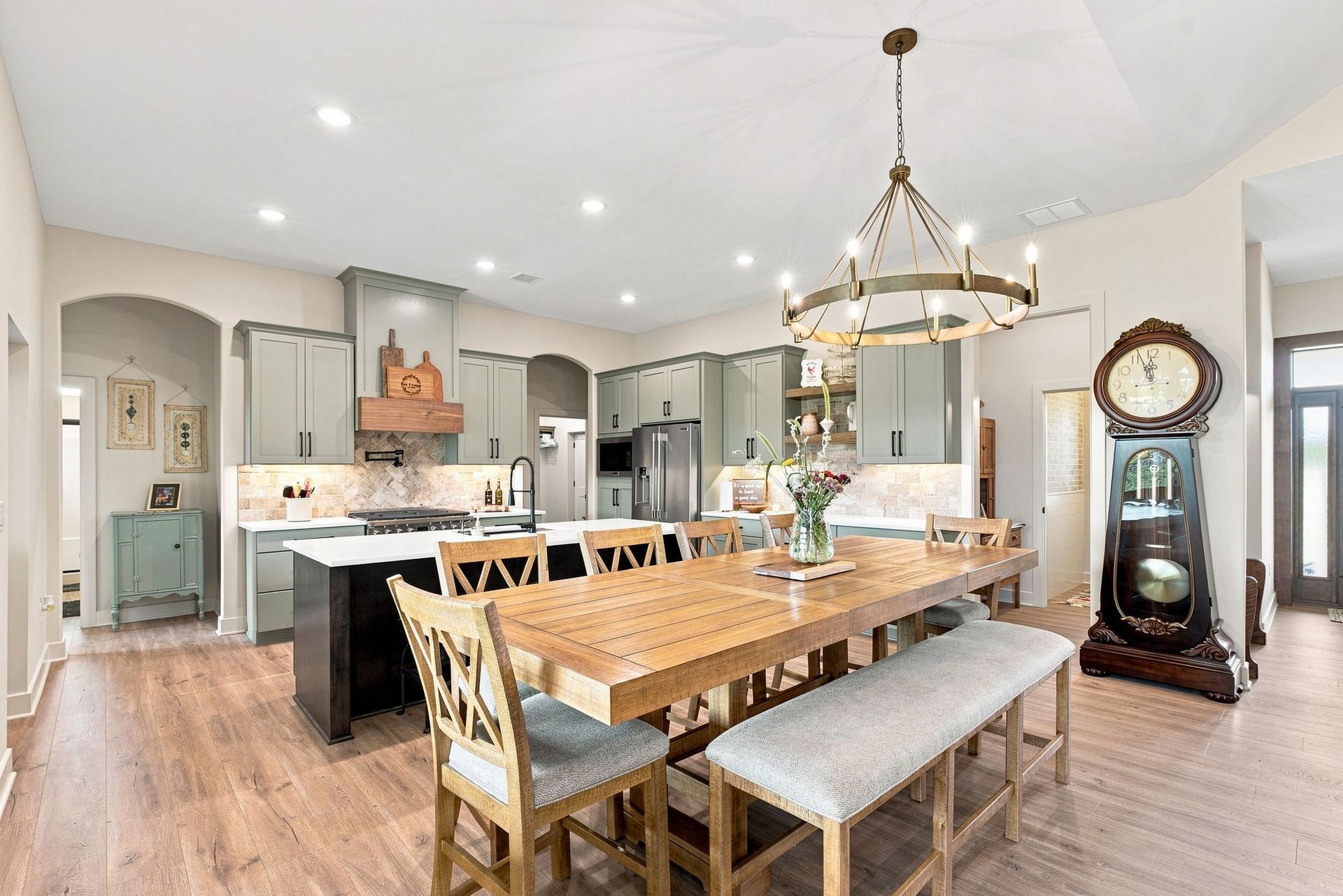 Bright open kitchen with island, wooden dining table, chandelier, and grandfather clock