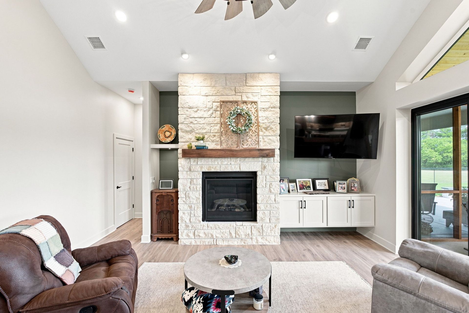 Bright living room with stone fireplace, wall-mounted TV, sofas, and large windows on the right.