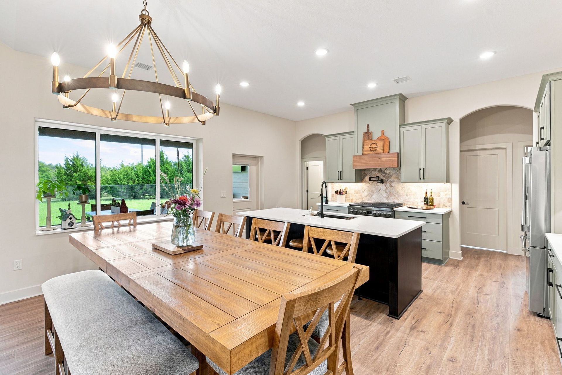 Bright modern kitchen and dining room with wood table, island, white cabinets, and large window view