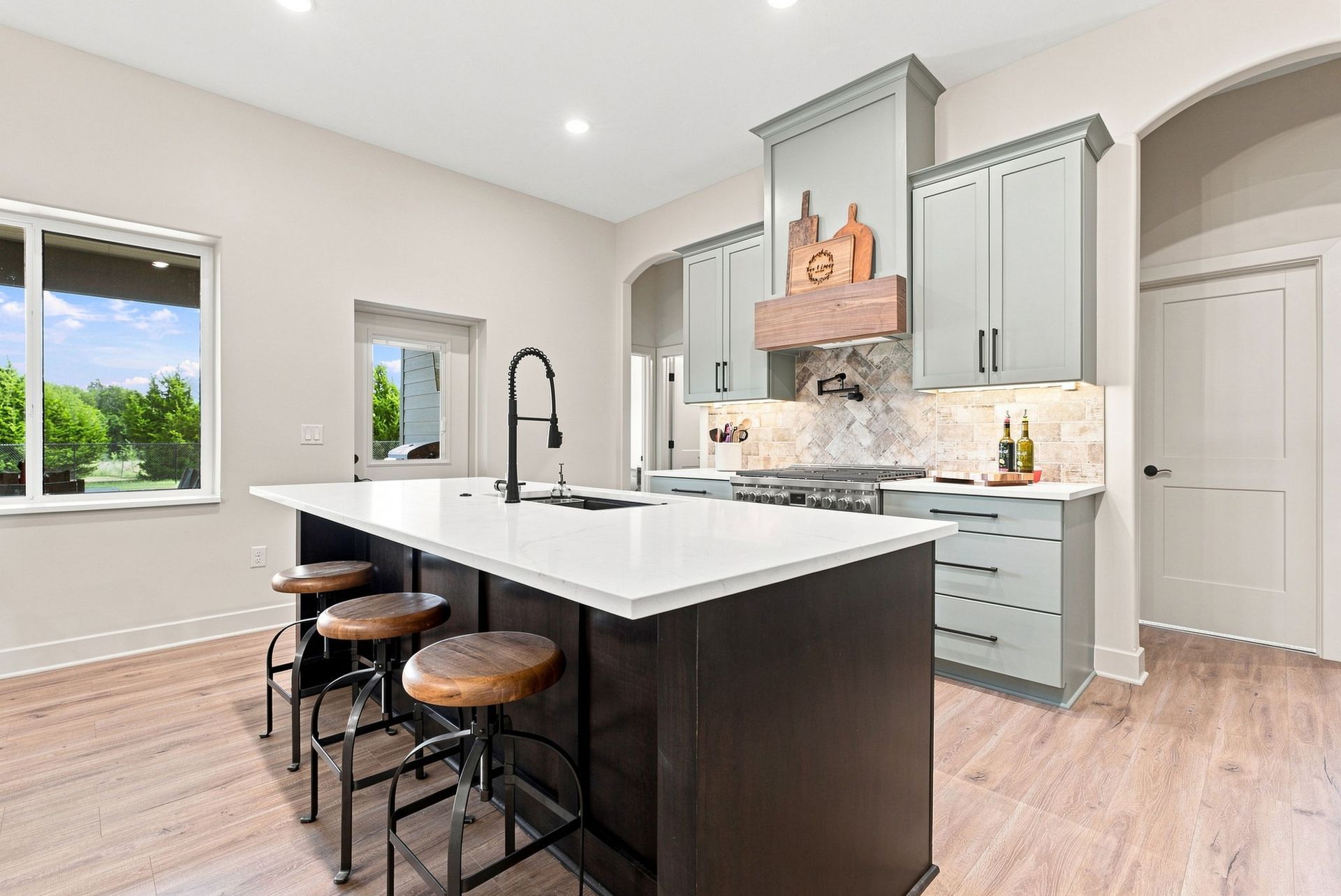 Bright modern kitchen with large island, gray cabinets, white countertops, and bar stools.