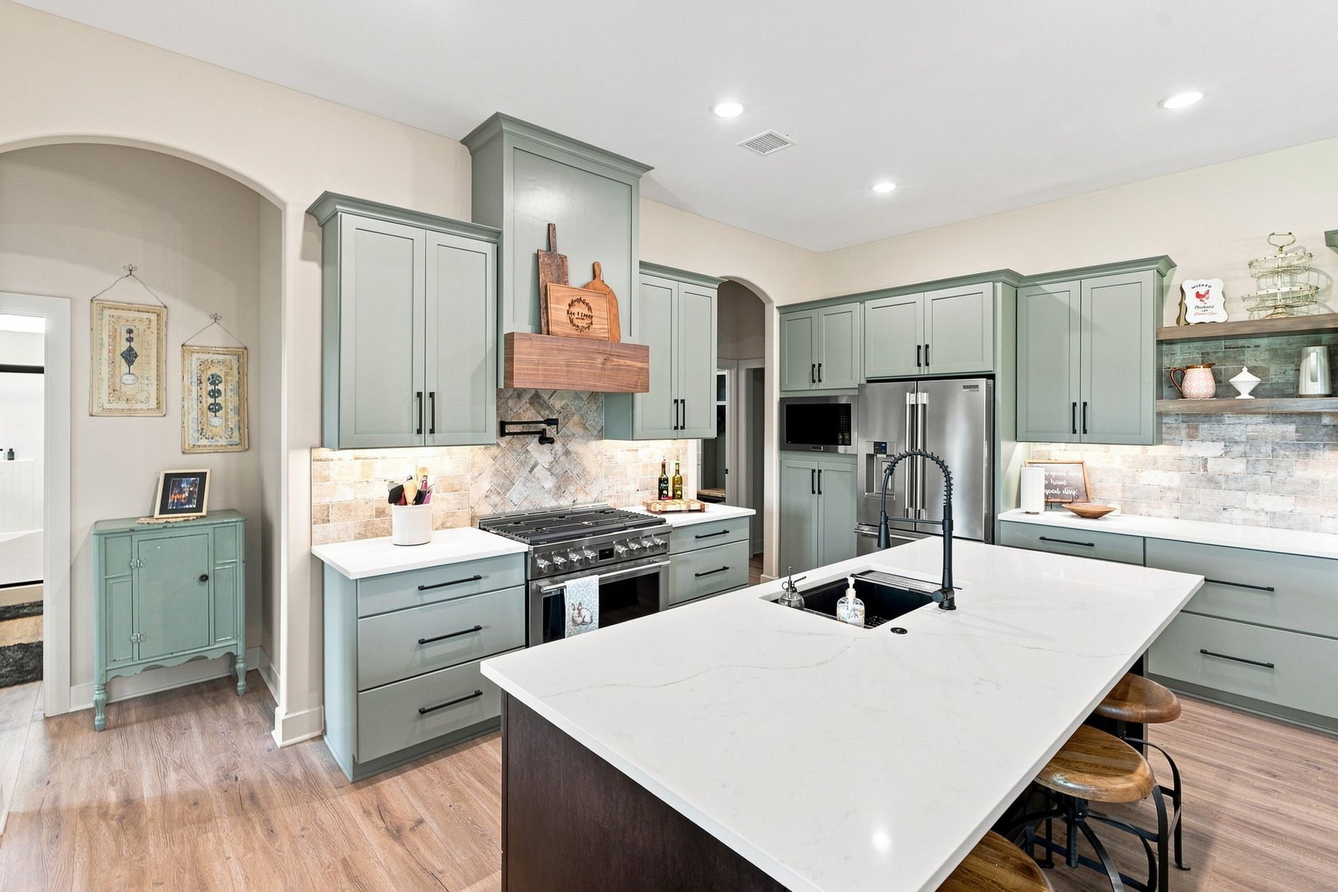 Bright modern kitchen with sage cabinets, white island, farmhouse sink, and copper range hood