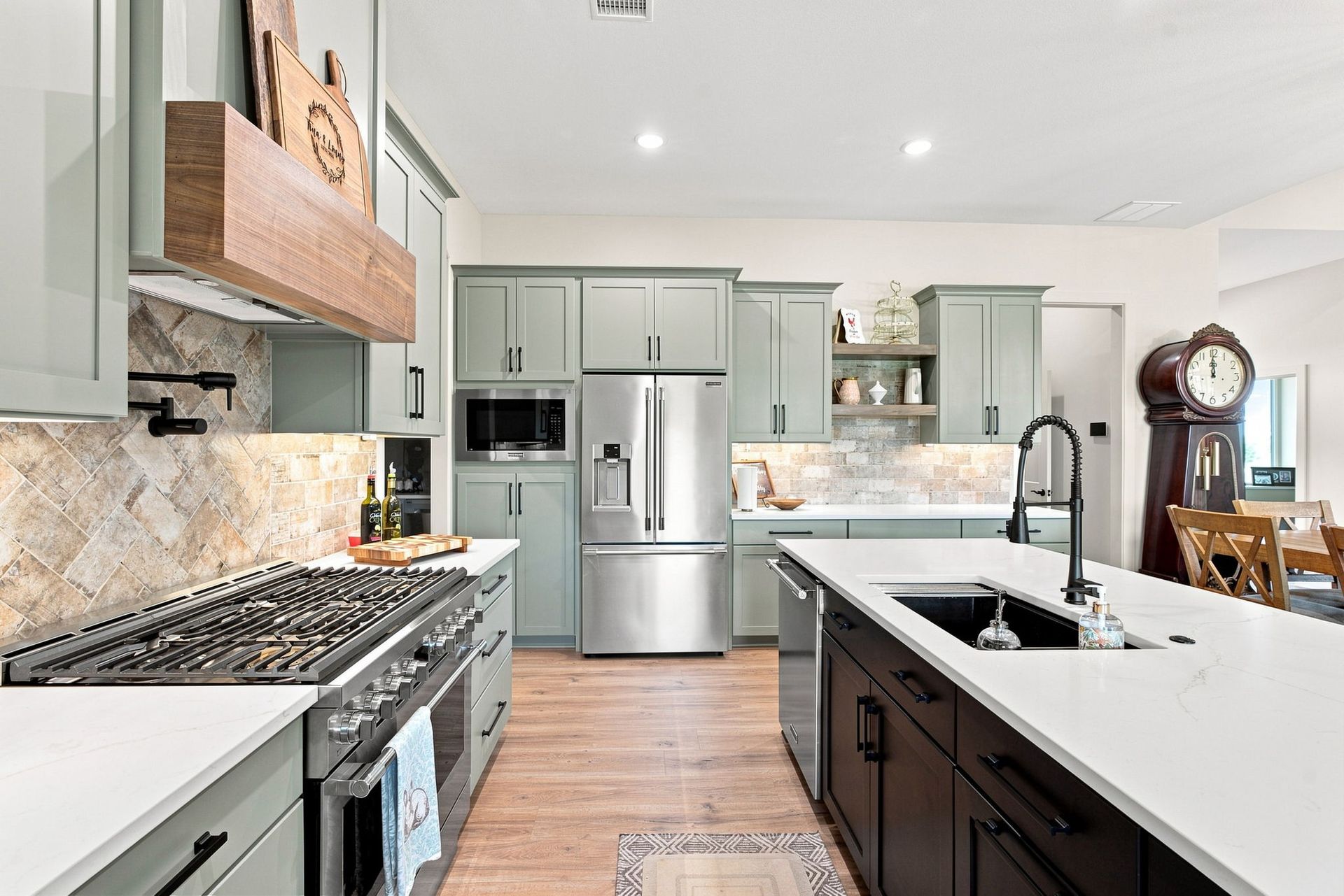 Bright modern kitchen with white counters, gray cabinets, stainless appliances, and a dark island.