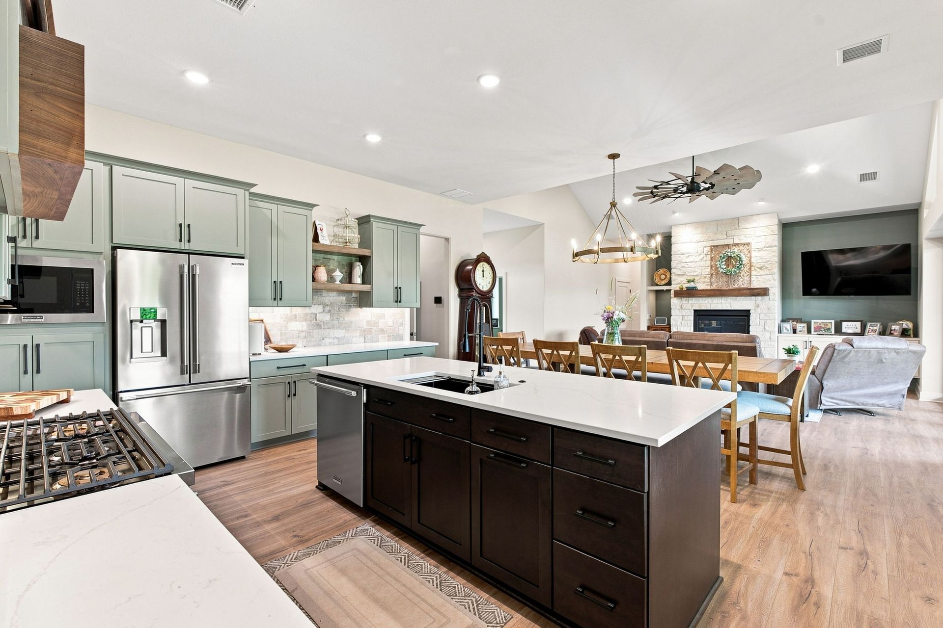 Modern open-plan kitchen and living area with white cabinets, dark island, stainless fridge, and TV fireplace.