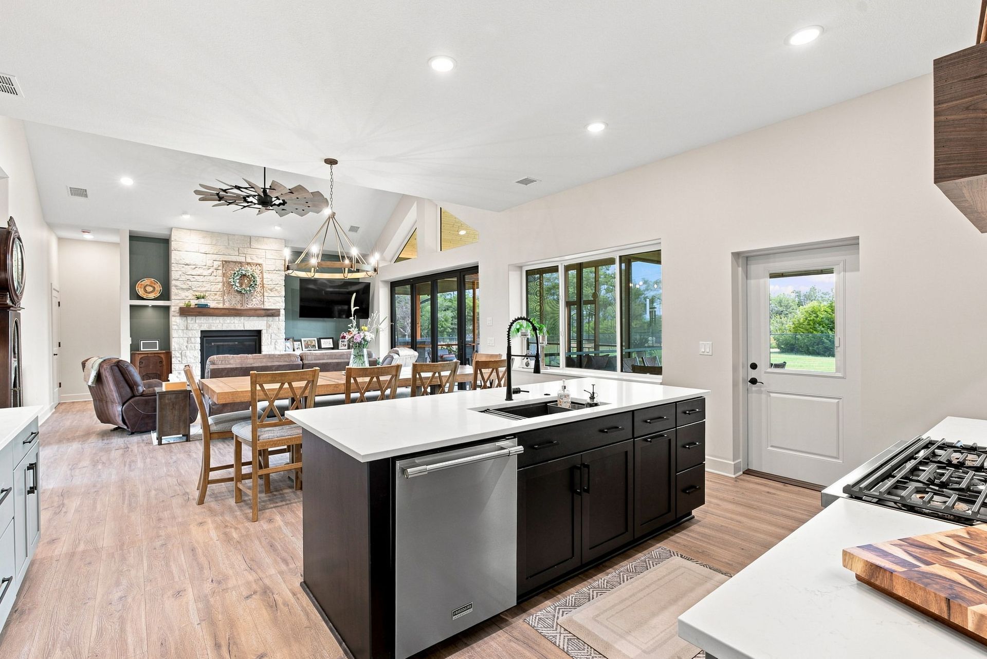 Bright modern kitchen with island, dark cabinets, white countertops, and dining area by large windows