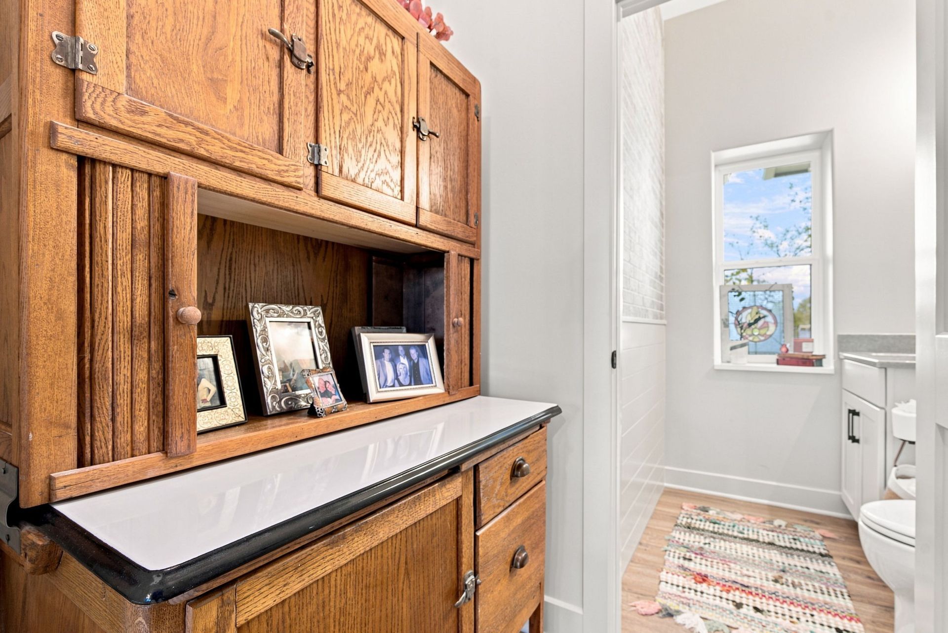 Bathroom vanity with wooden cabinets, a sink counter, framed photos, and a toilet by a window.