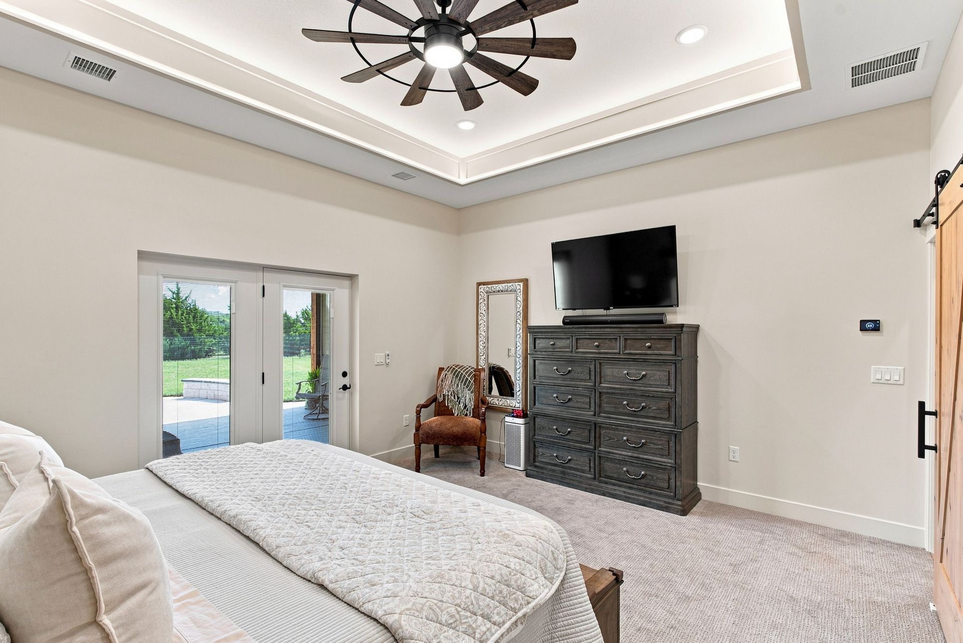 Bright bedroom with a ceiling fan, dresser and TV, French doors, and a bed with white bedding.