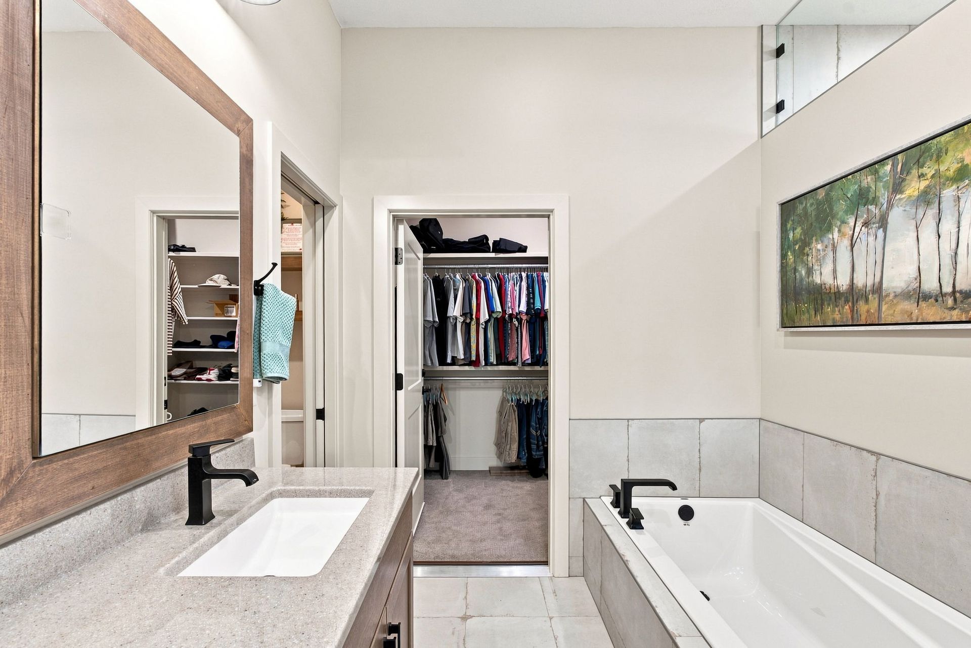Bright bathroom with double vanity, open closet, and white tub with tree artwork on the wall