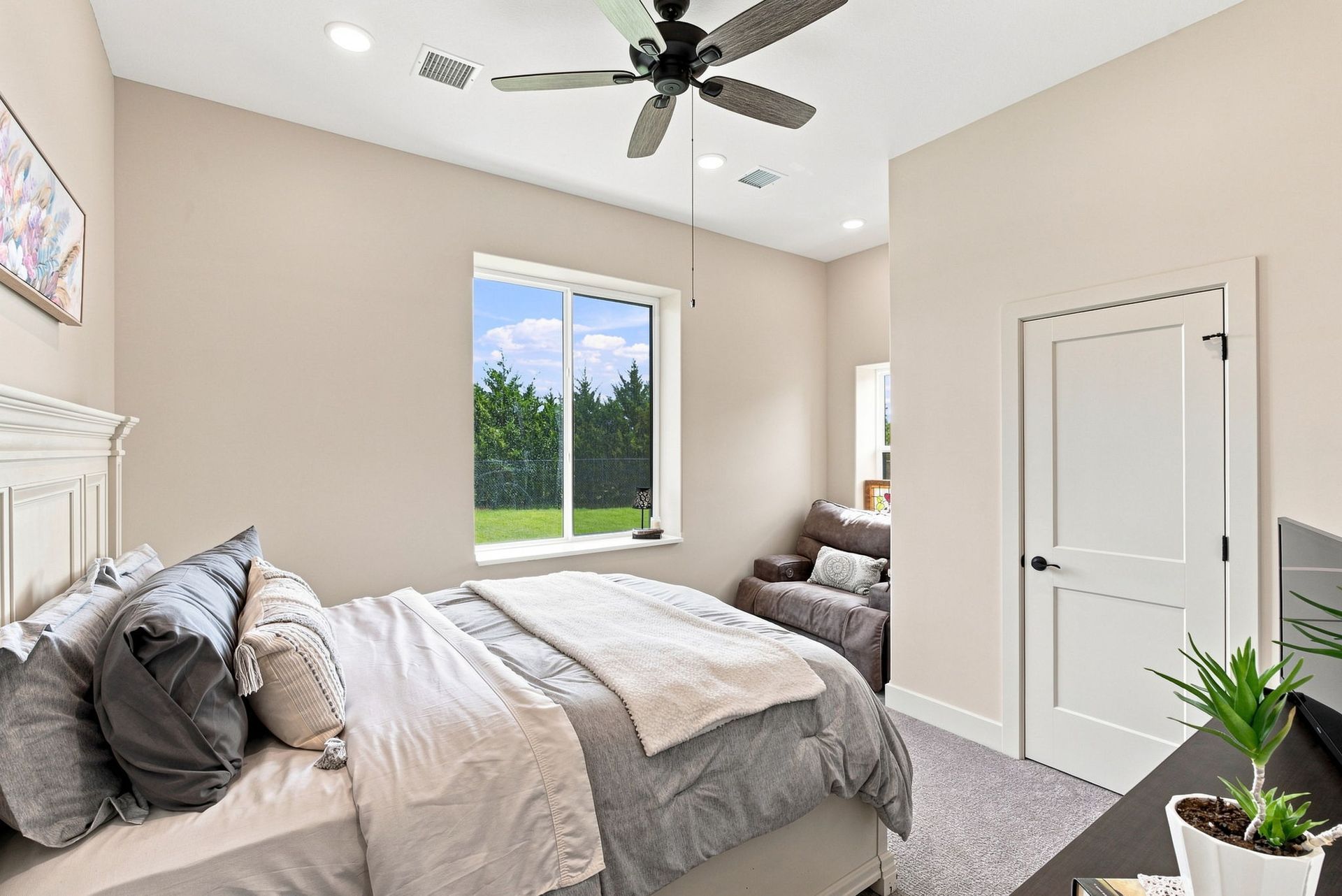 Bright bedroom with a bed, ceiling fan, and large window overlooking a green yard