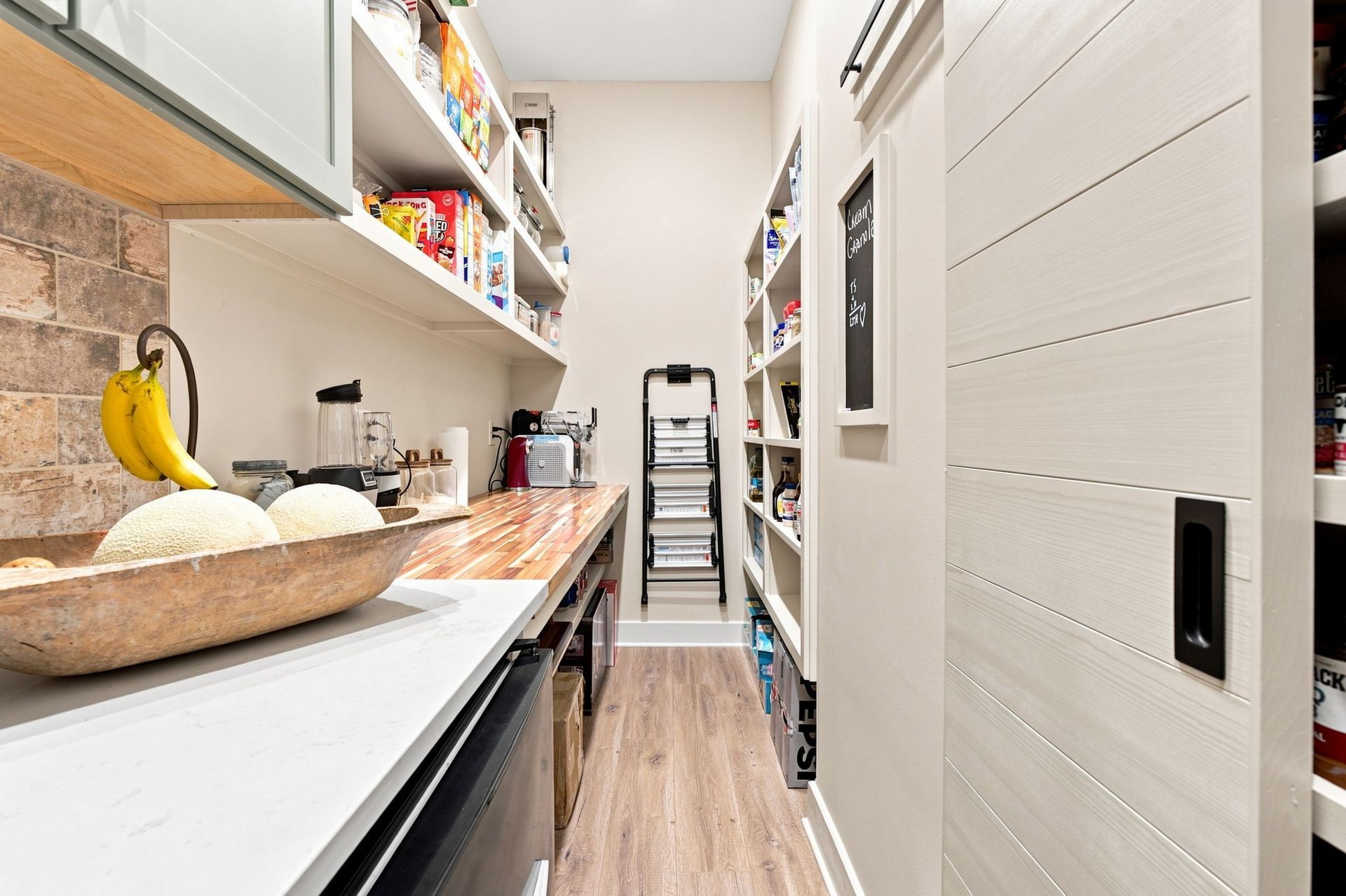 Narrow pantry with shelves of snacks, bananas on the counter, and a white sliding door.