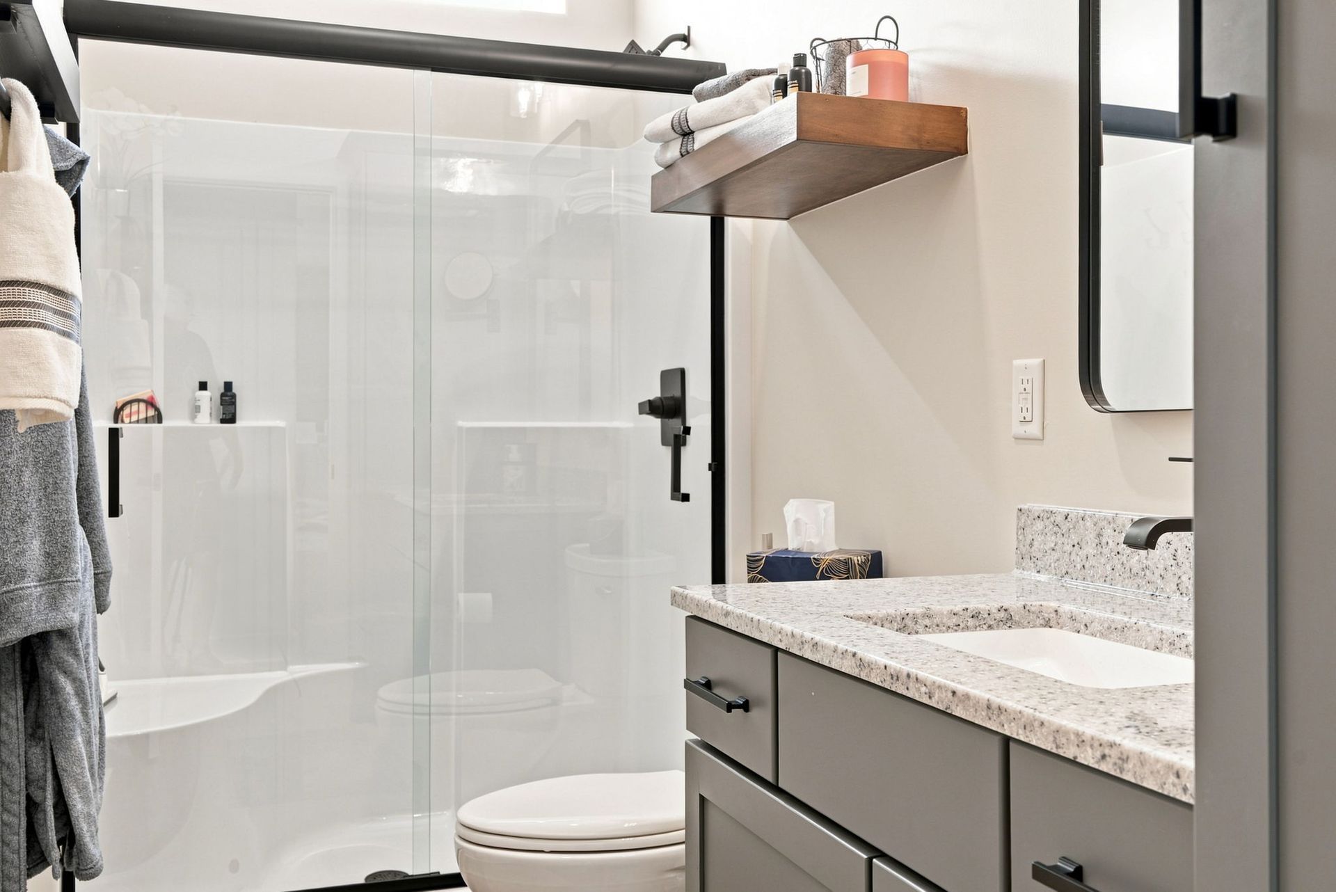 Modern bathroom with glass shower, toilet, granite vanity, and wall mirror