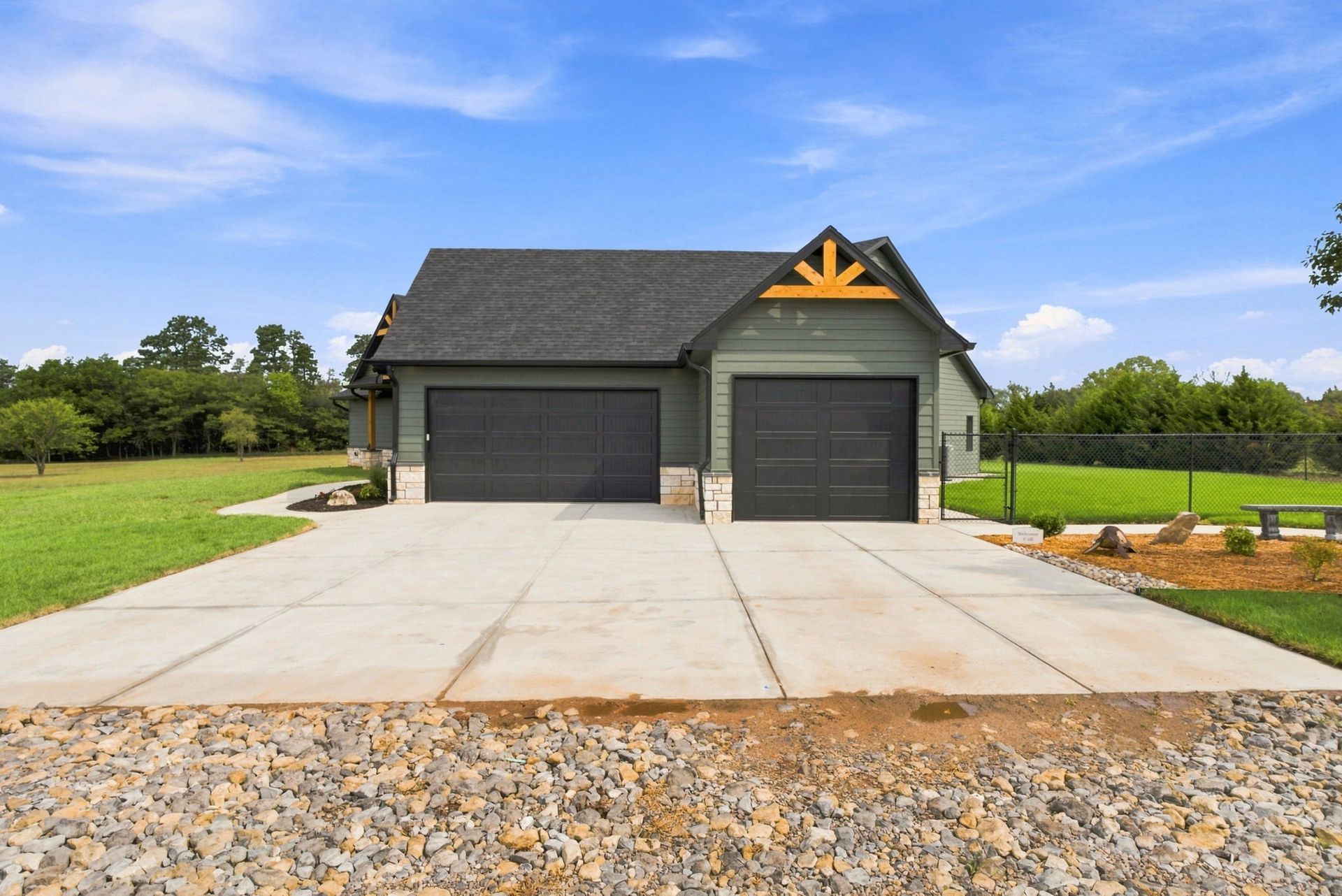 Modern gray garage with three doors and a large concrete driveway under a blue sky.