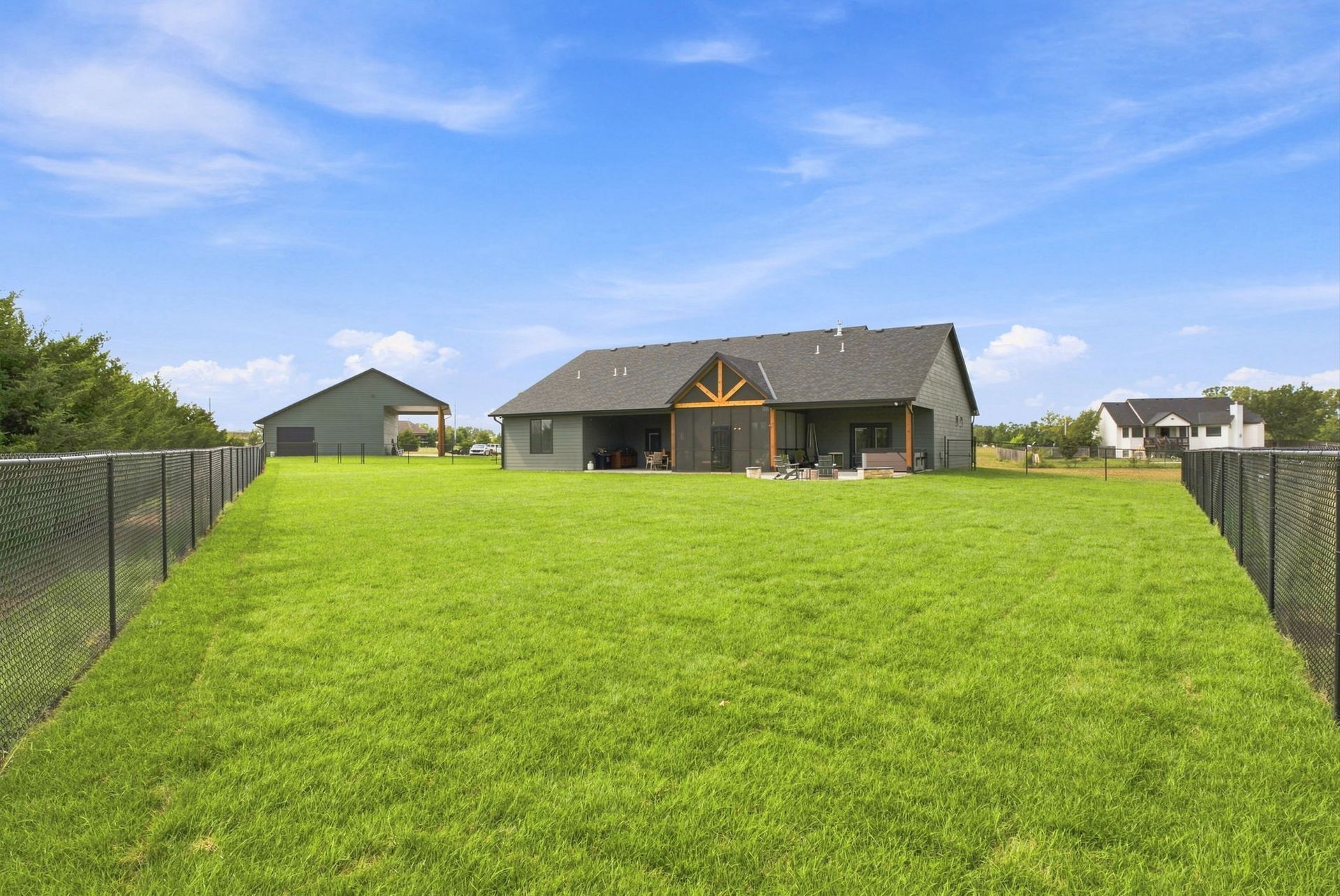 Wide green backyard with a fenced lawn and a house under a blue sky