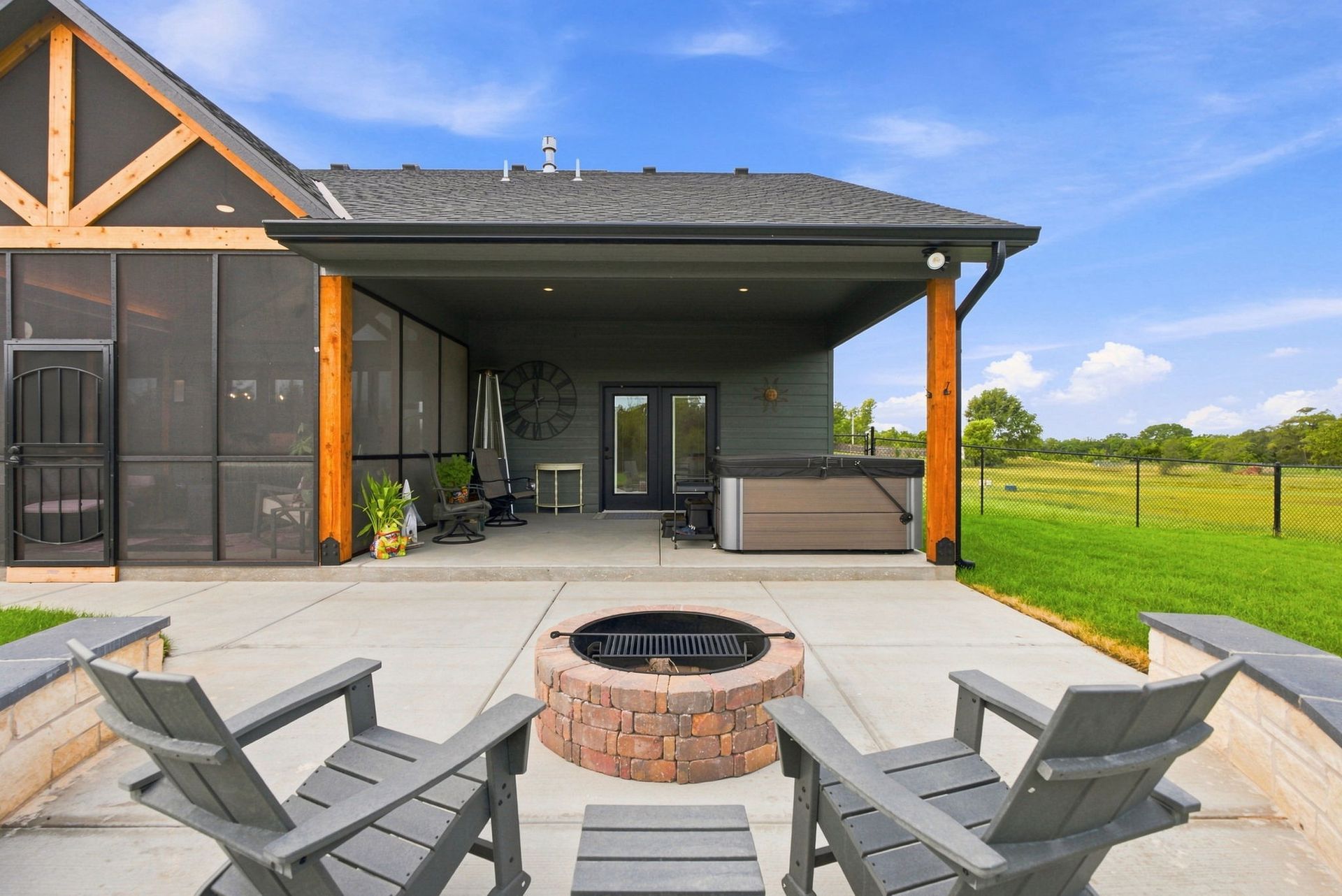 Modern patio with fire pit and gray chairs beside a covered porch and green lawn