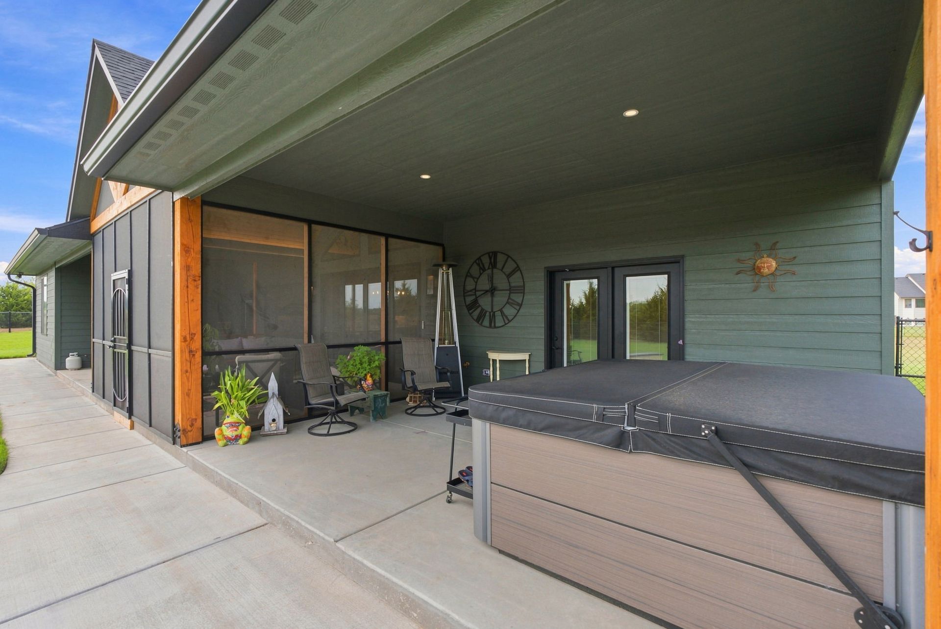 Covered patio with sliding glass doors, outdoor seating, and a hot tub beside a modern house
