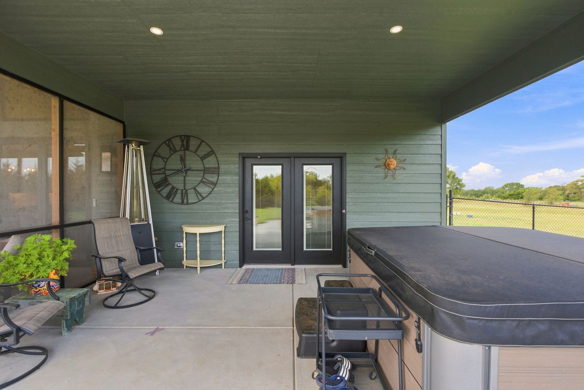 Covered patio with lounge chairs, wall clock, and a hot tub overlooking a grassy yard