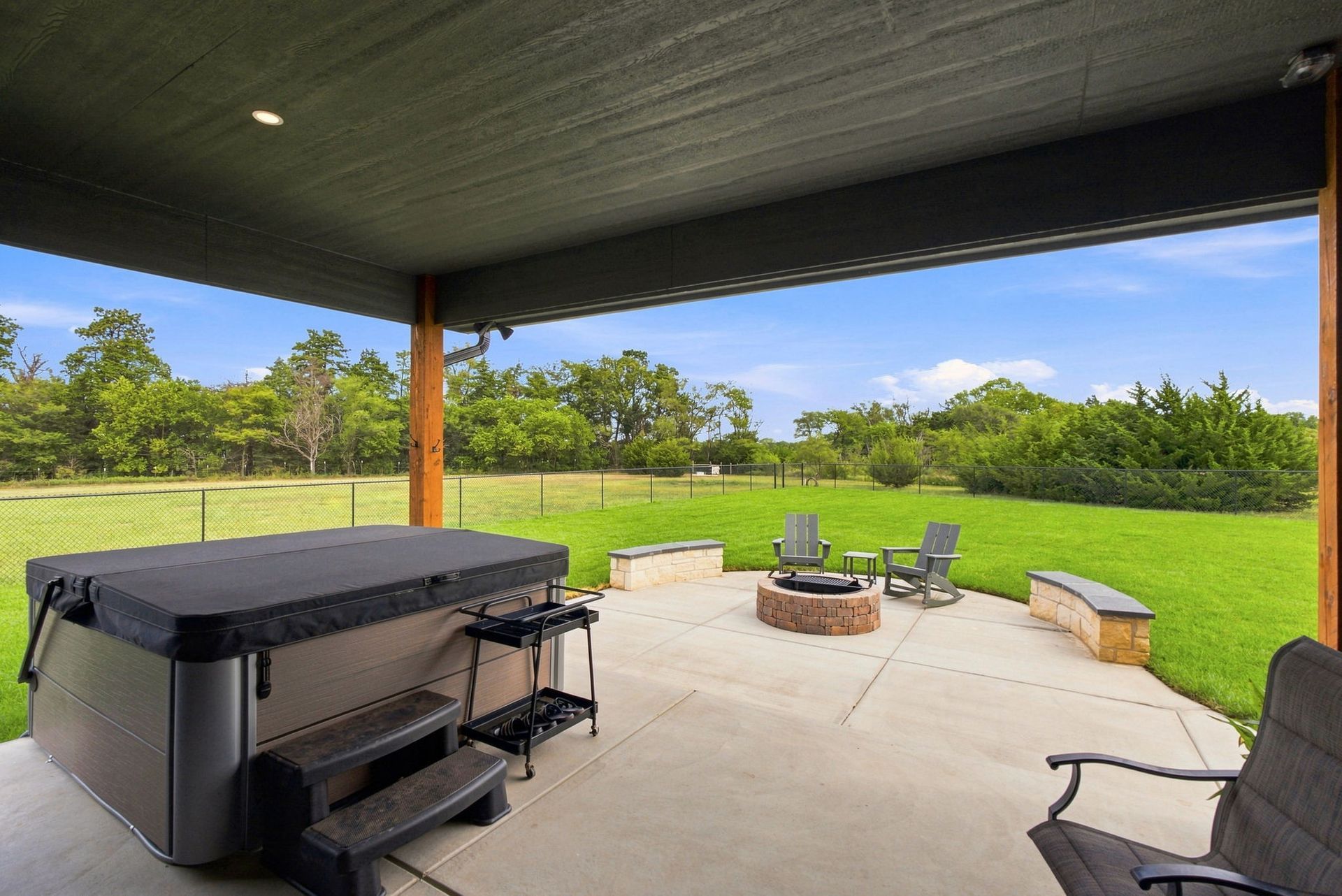 Covered patio with grill, fire pit seating, and a green backyard view under a dark roof.