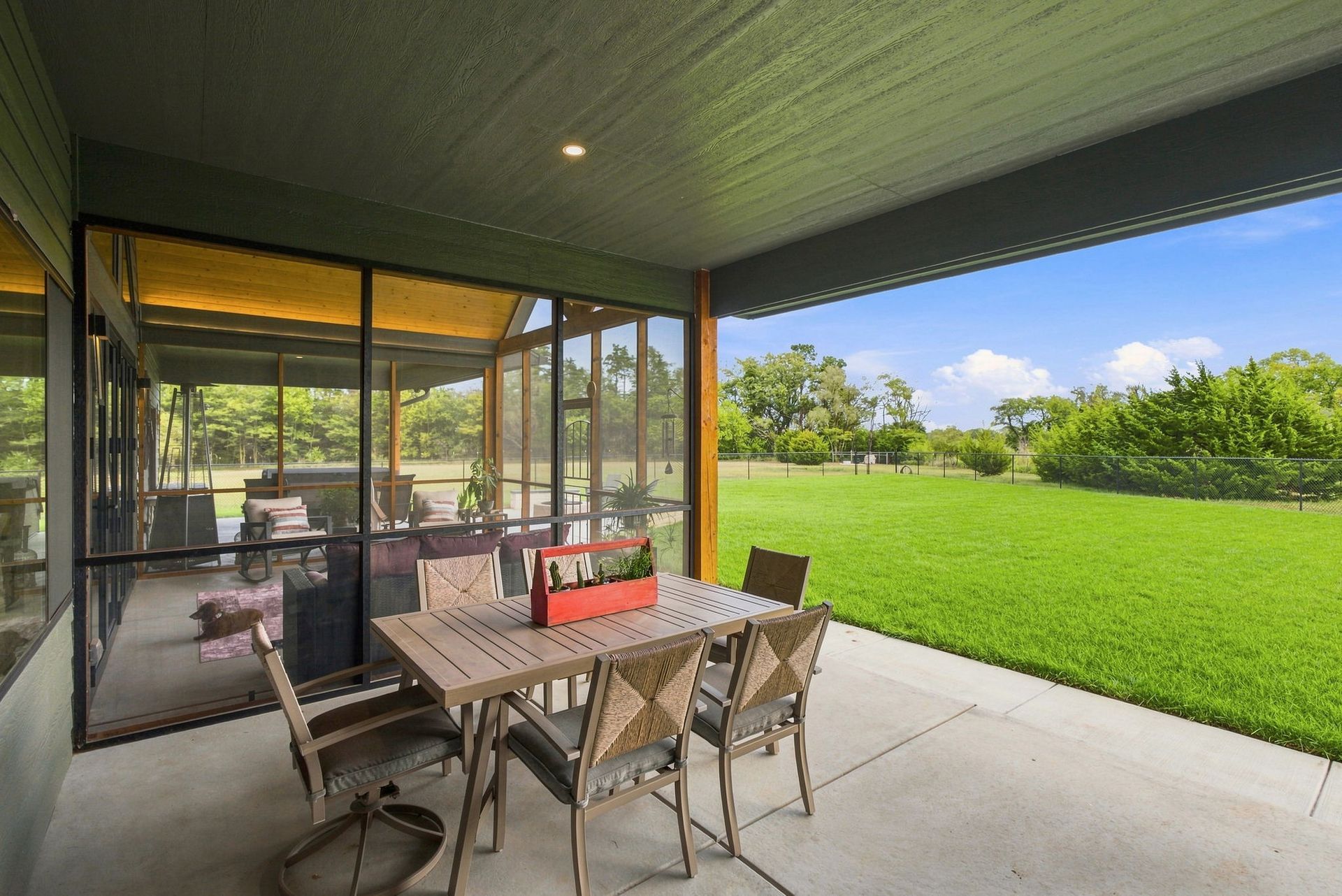 Covered patio with dining table and chairs overlooking a bright green lawn