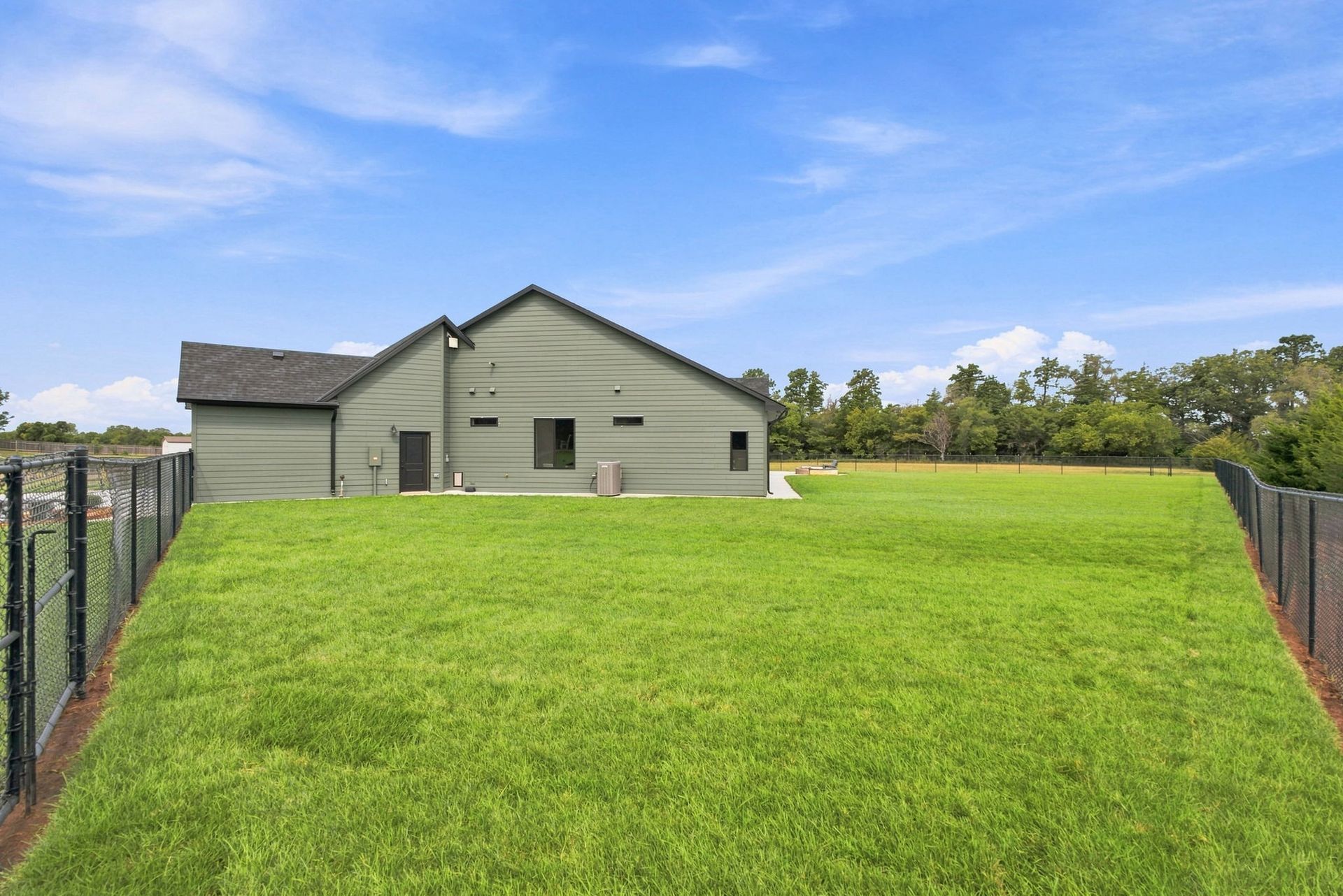 Grassy backyard leading to a light gray house beneath a blue sky