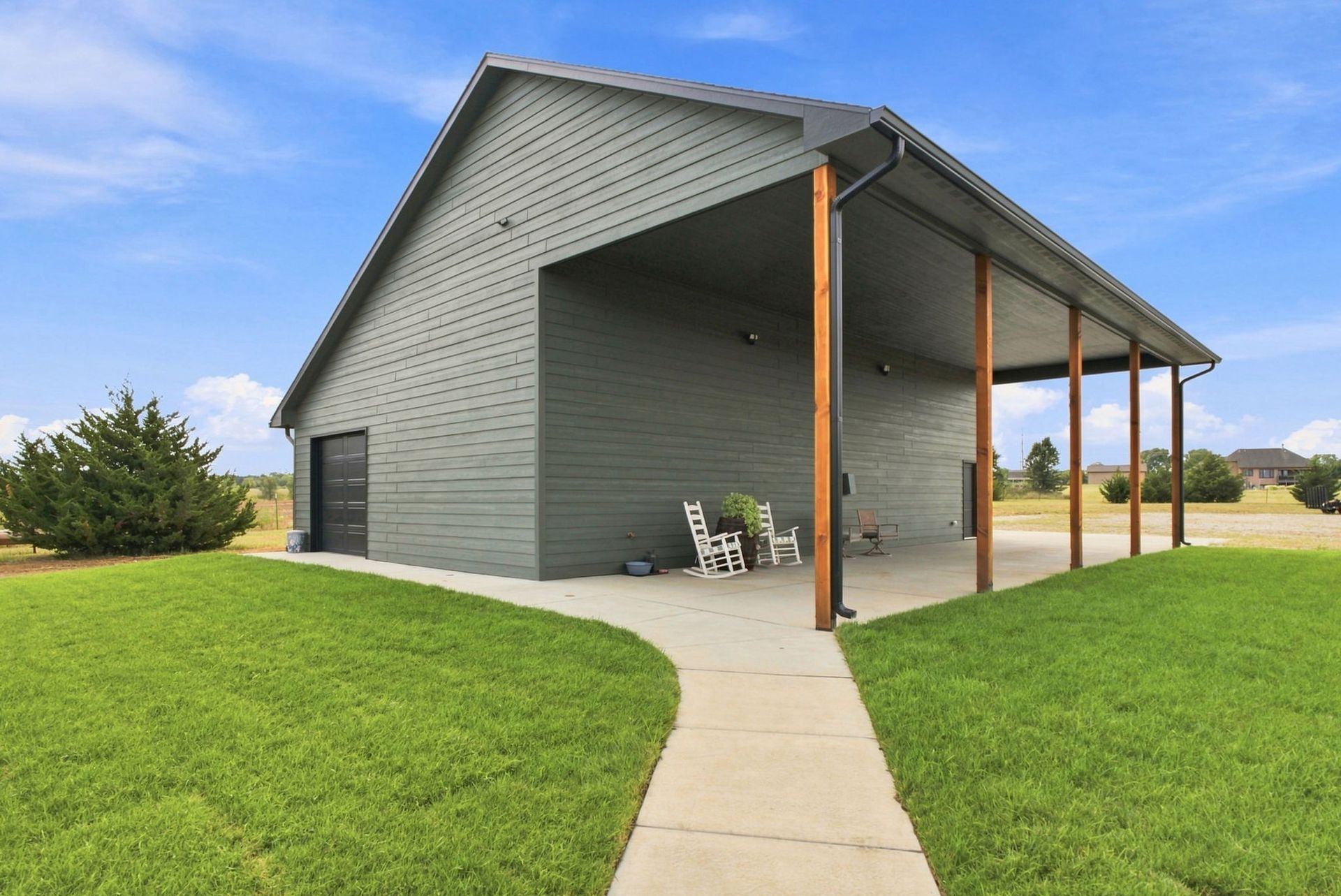 Gray barn-style pavilion with a covered patio, green lawn, and a sidewalk leading to the entrance