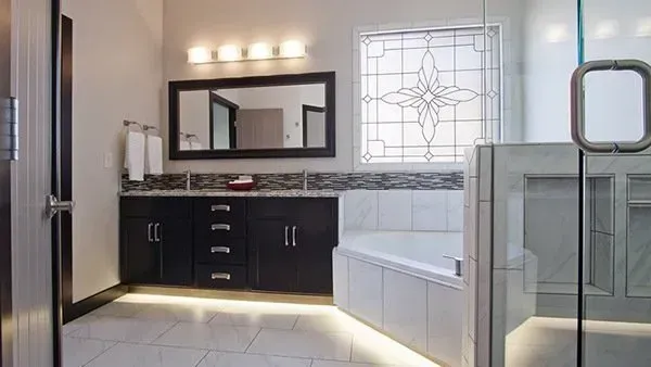 Modern bathroom with dark vanity, large mirror, white bathtub, and glass shower enclosure