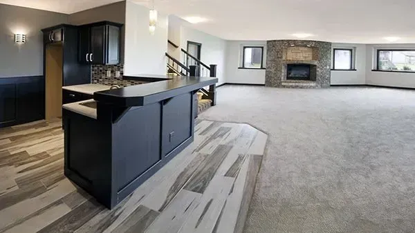 Open-concept living room and kitchen with dark cabinets, gray carpet, and a stone fireplace.