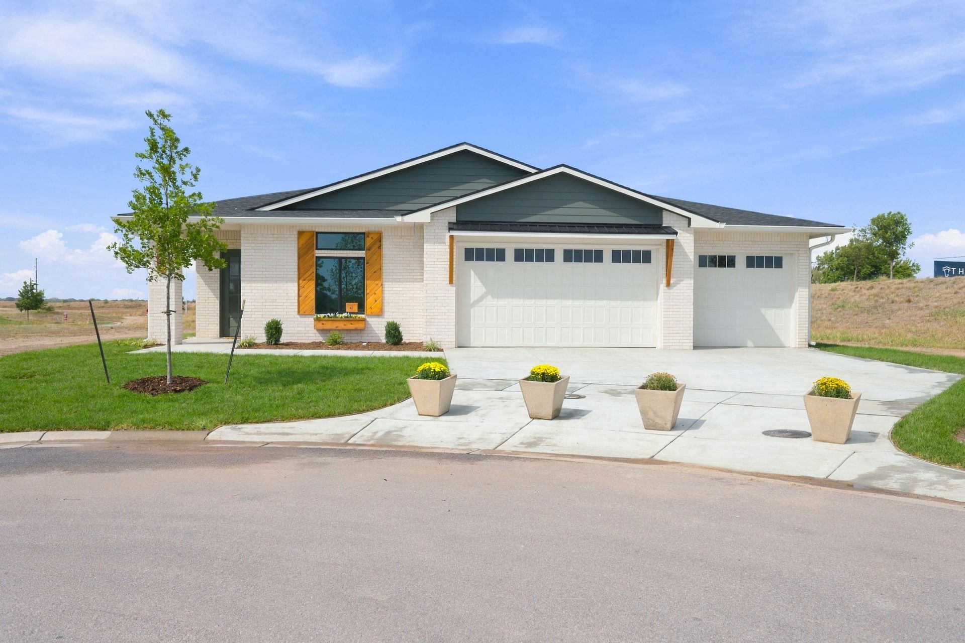 Modern single-story house with gray roof, white garage doors, and small front yard with potted plants.