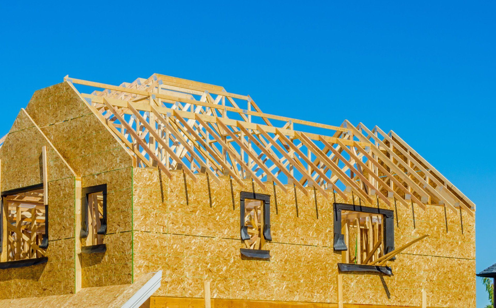 Partially framed house with exposed wooden roof trusses under a clear blue sky