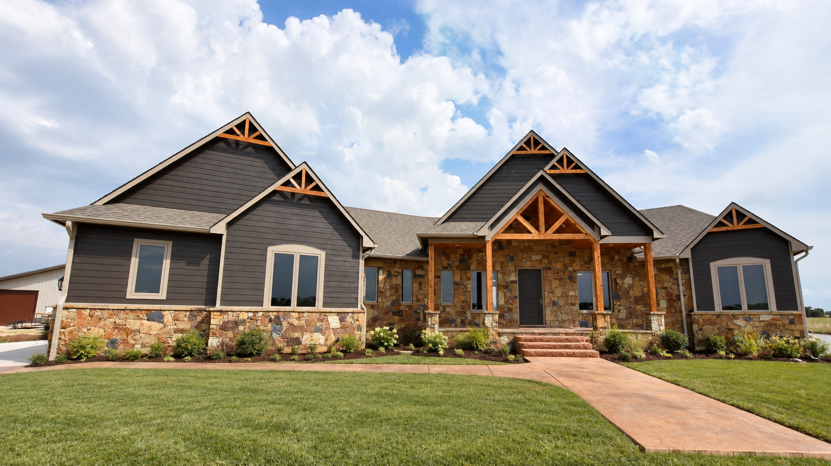 Modern dark-gray house with stone accents, wood trim, front porch, and a manicured lawn under a cloudy sky