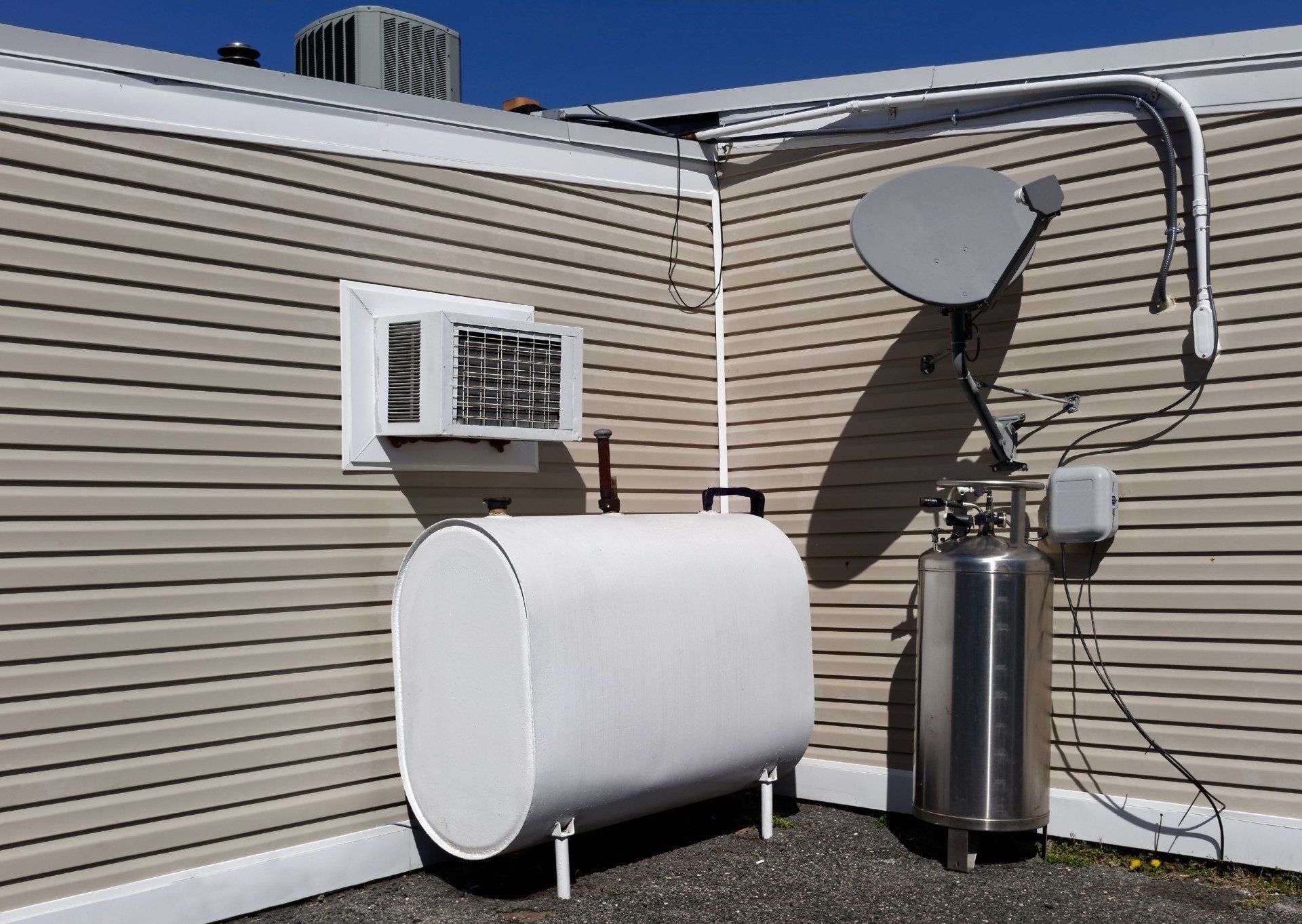 White fuel oil tank and tall, silver tank with satellite dish on a building exterior.