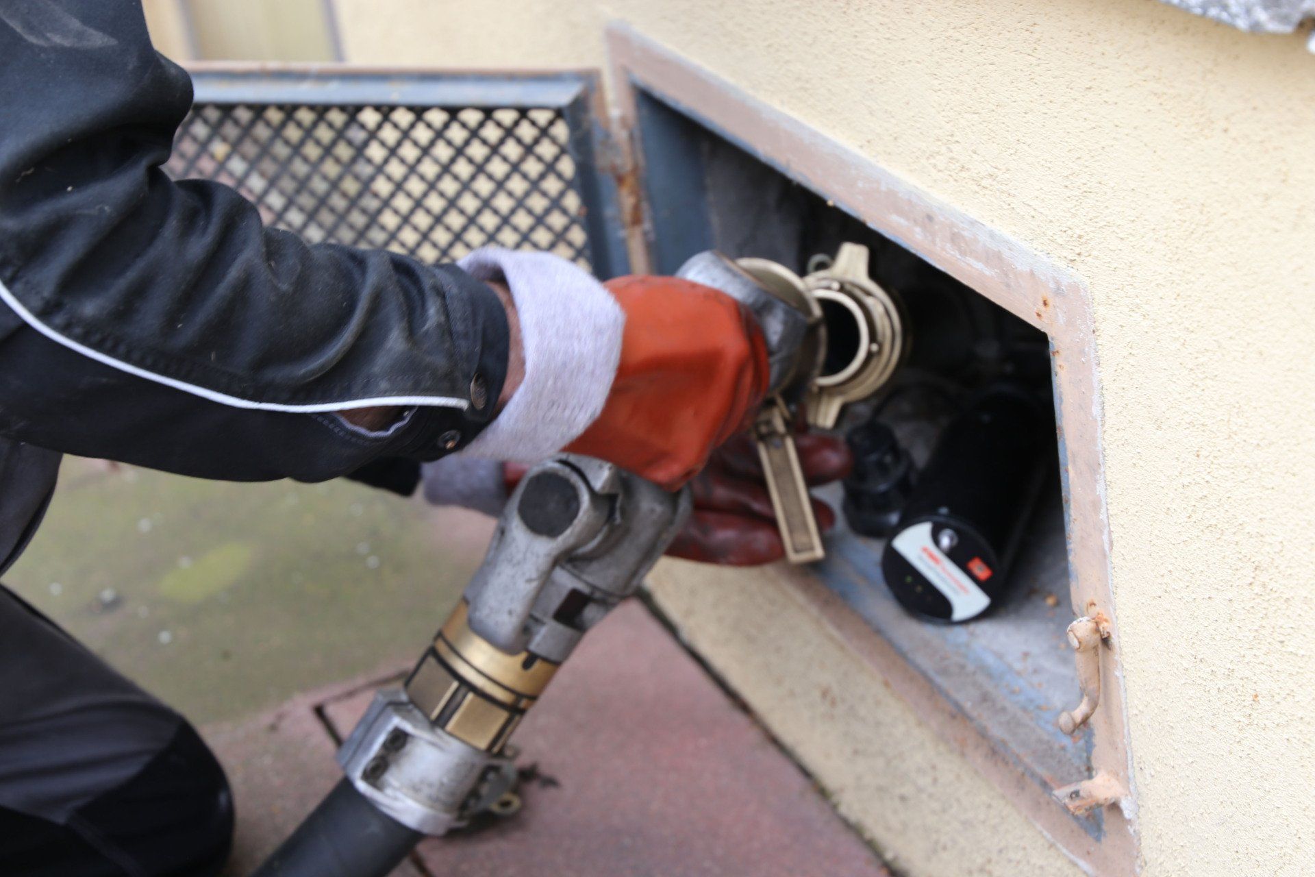 Person in work gloves connecting a hose to a fuel tank inside a wall.