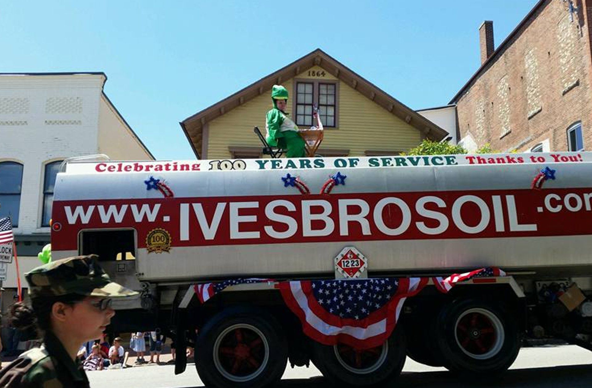 Oil tanker with a person on top in a green outfit, advertising Ives Bros Oil, at a parade.