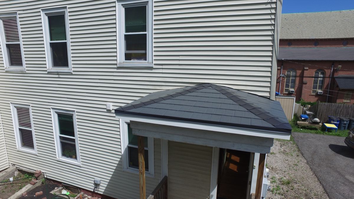 Side view of a beige house with white trim and a small covered porch roof.