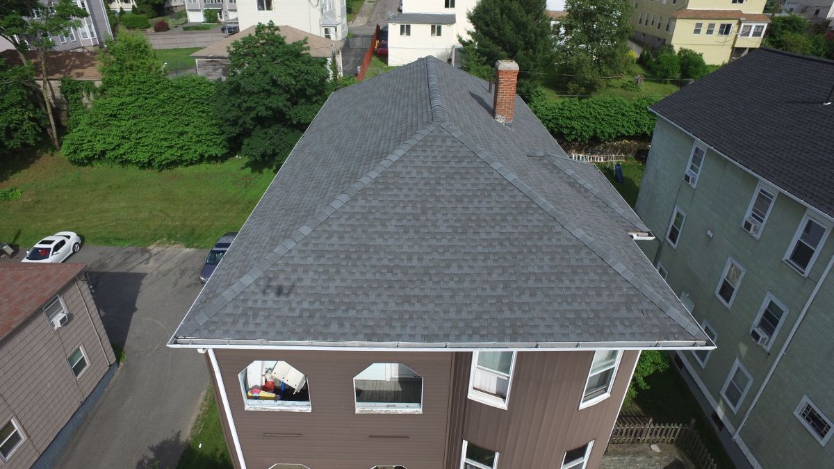Aerial view of a house with a gray shingled roof and brick exterior in a suburban neighborhood